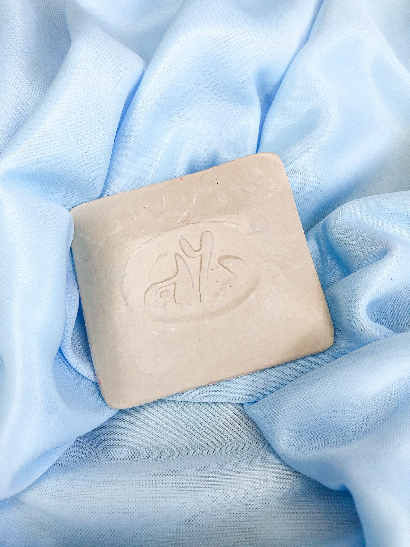 Sabonete quadrado bege com desenho em relevo sobre tecido azul claro