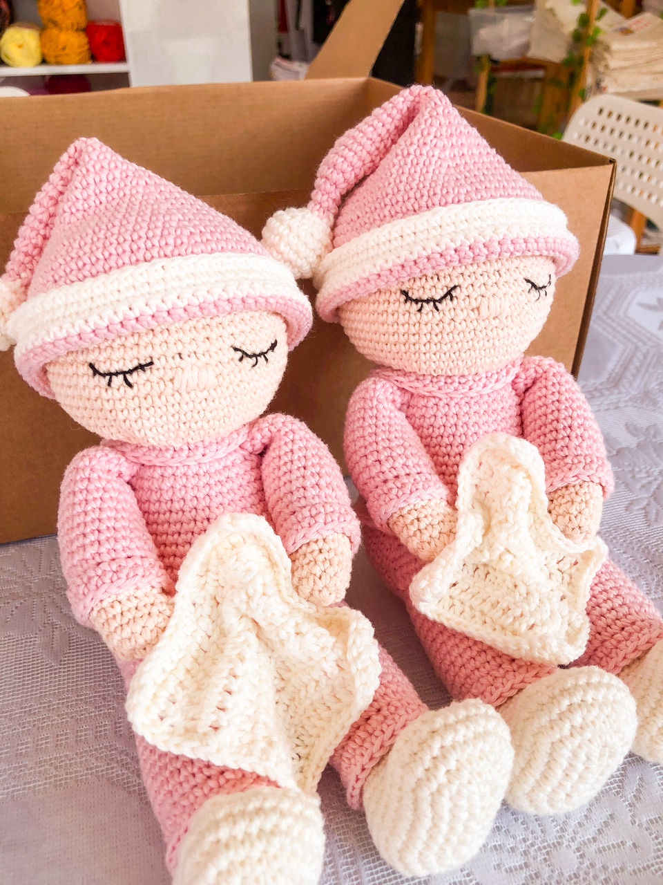Dois bonecos de croché cor-de-rosa com toucas e mantas brancas