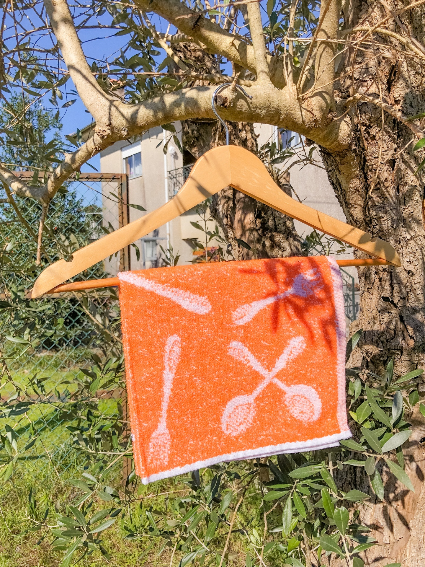 Toalha laranja com padrão de colheres pendurada em cabide de madeira numa árvore