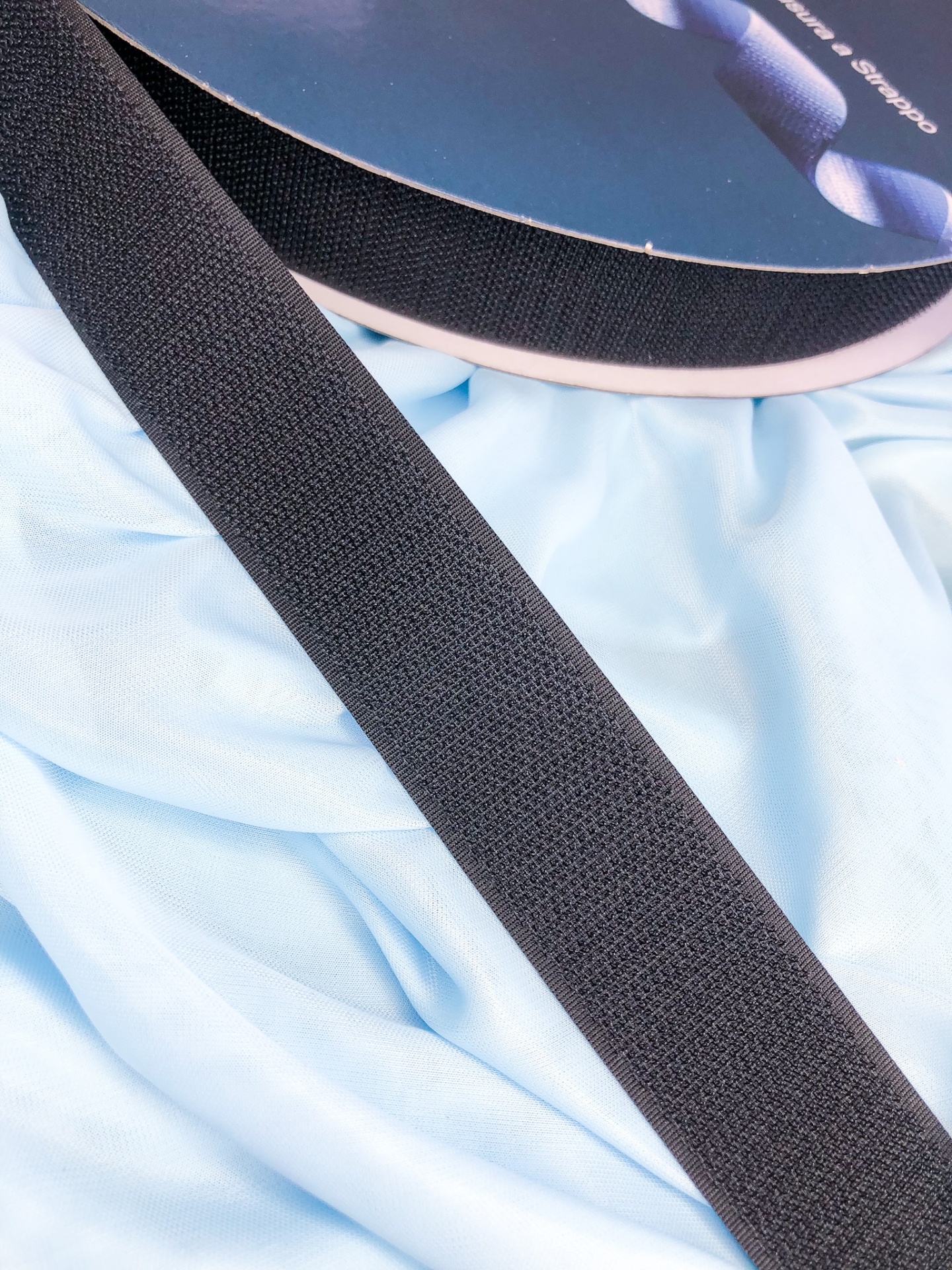 Fita de velcro preta sobre tecido azul claro com rolo de fita preta ao lado