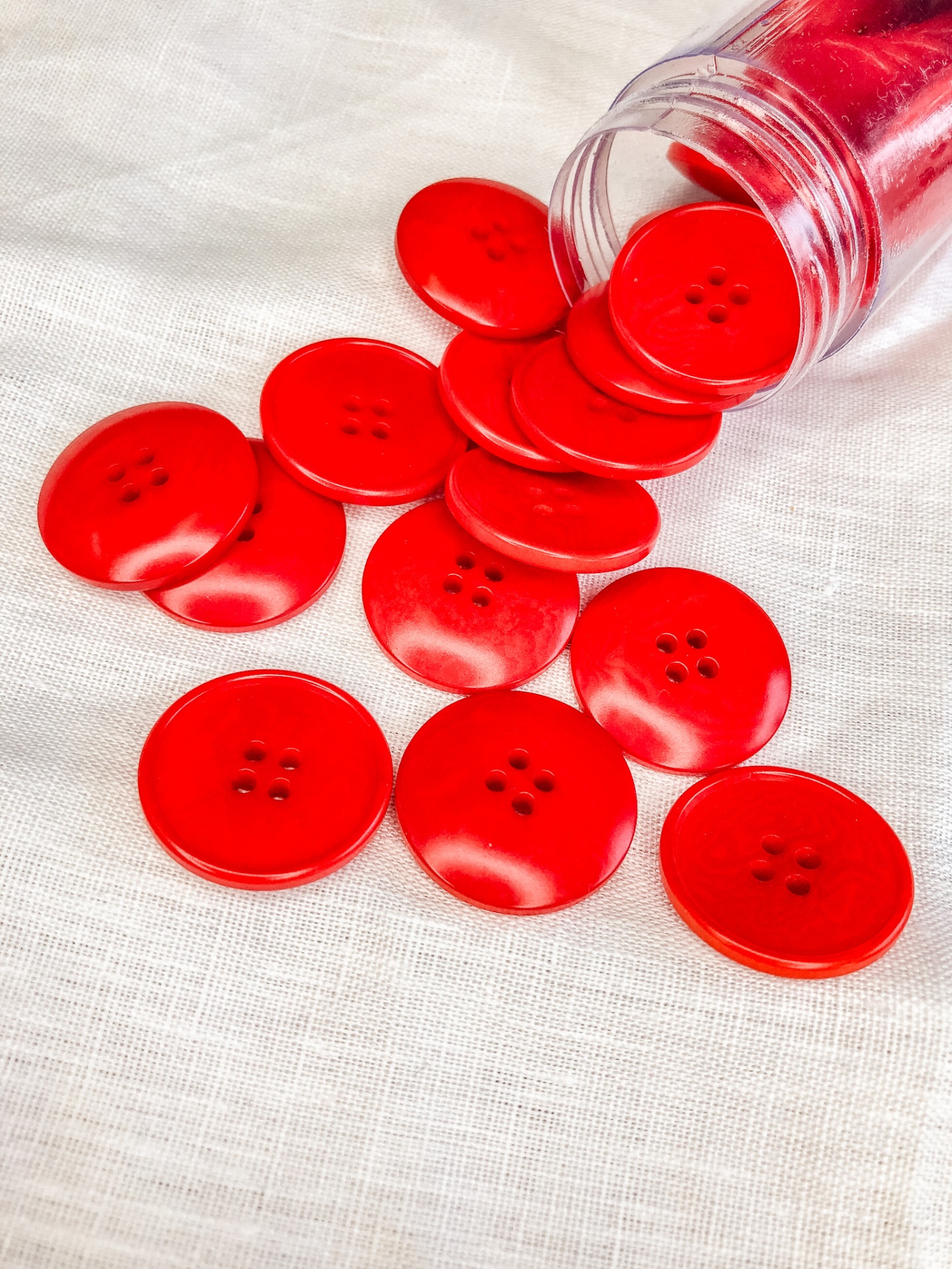 Botões vermelhos grandes com quatro orifícios em tecido branco e frasco plástico