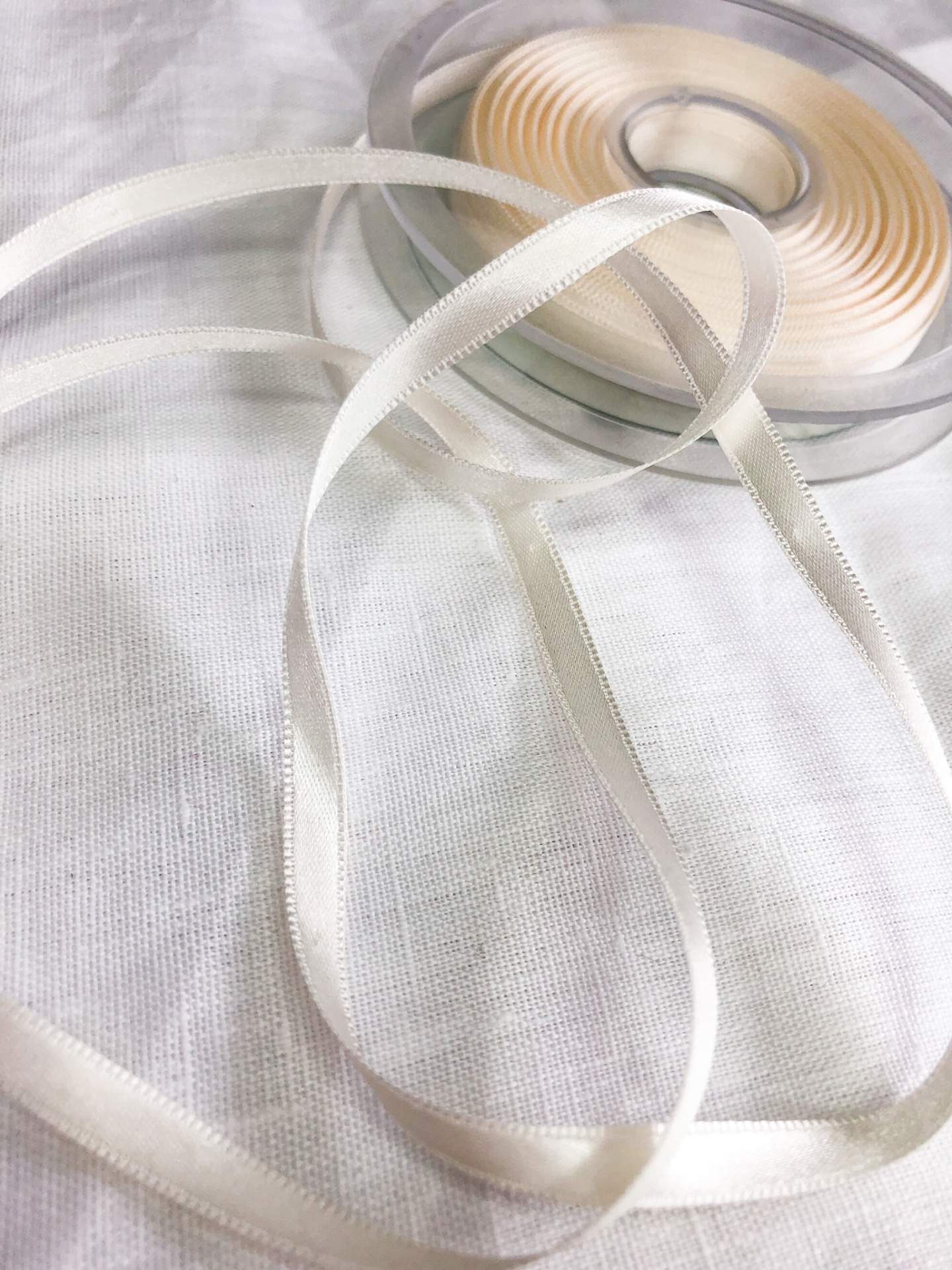 Rolo de fita de cetim branca fina sobre tecido branco