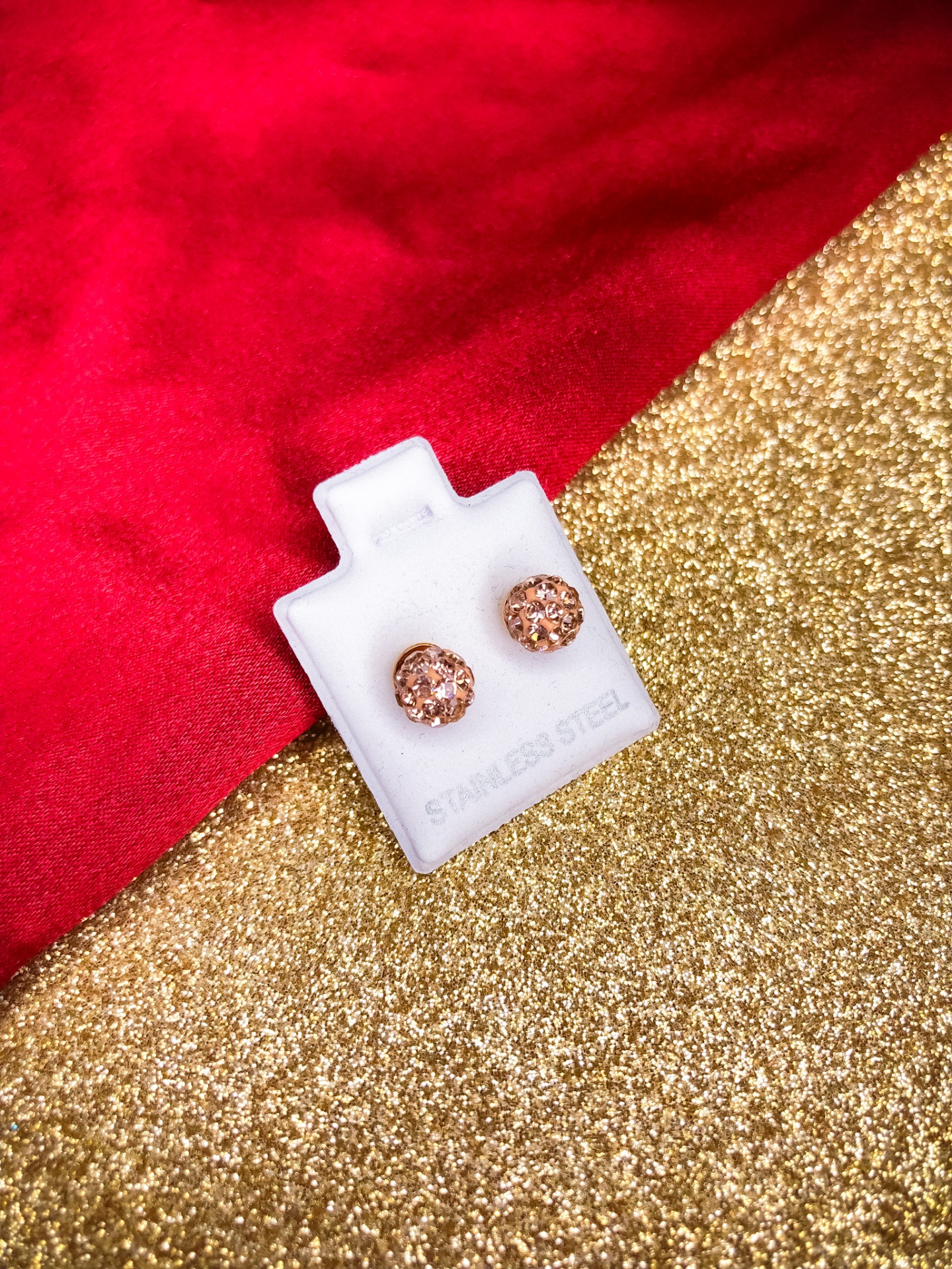 Brincos redondos cor de rosa em suporte branco sobre fundo dourado e vermelho