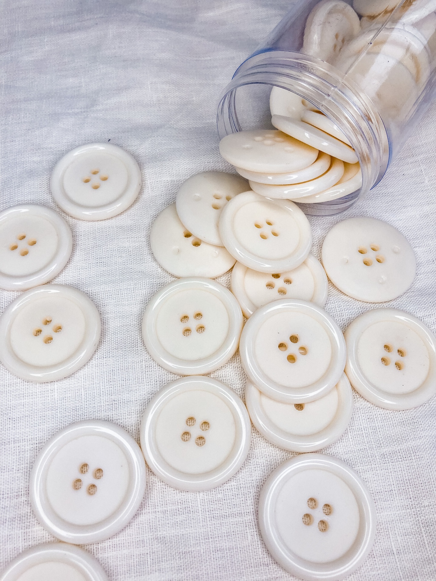 Botões brancos redondos com quatro furos em tecido branco e frasco plástico aberto