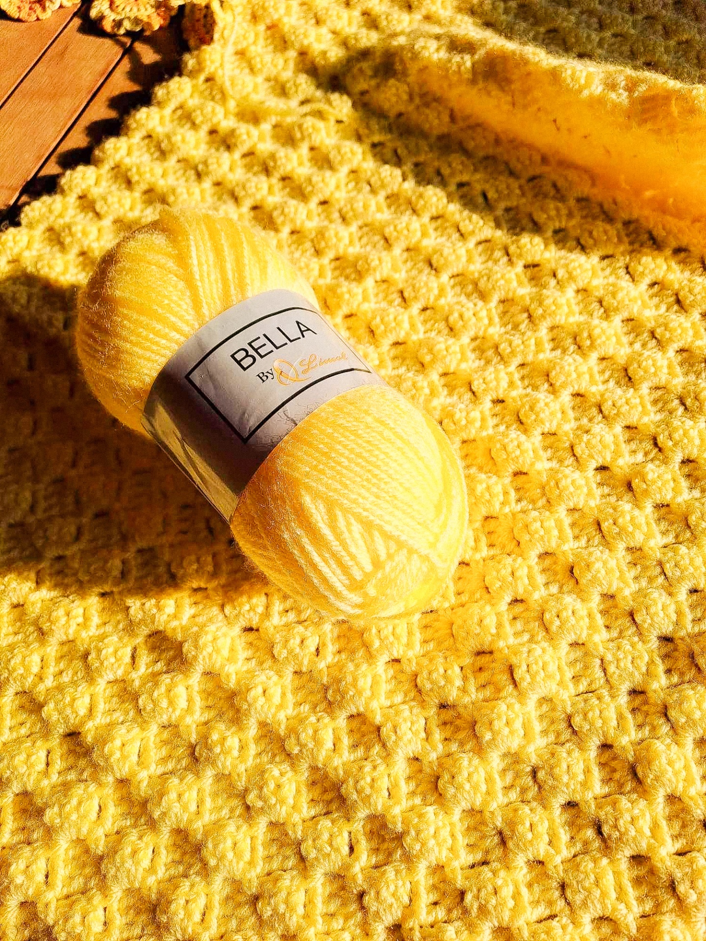 Novelo de fio amarelo com etiqueta sobre manta amarela texturizada em madeira