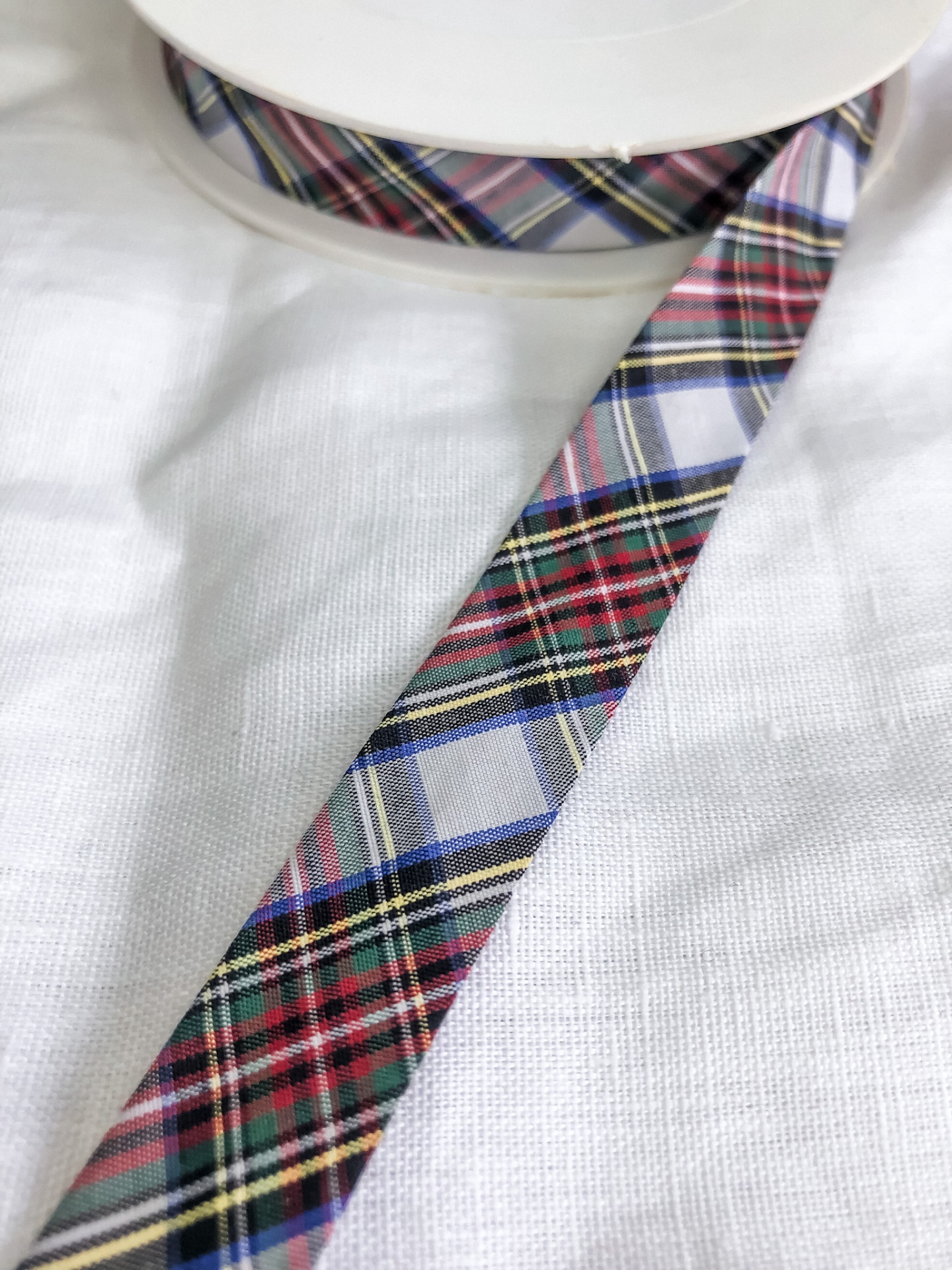 Rolo de fita decorativa xadrez colorida sobre tecido branco.