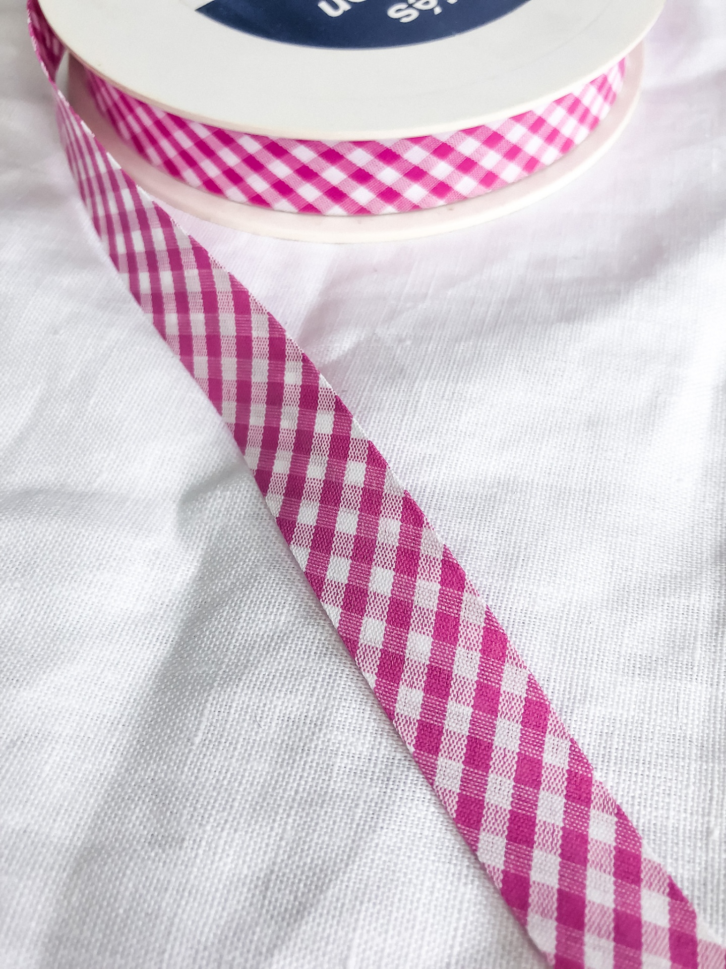 Fita decorativa xadrez rosa e branco num carretel sobre tecido branco