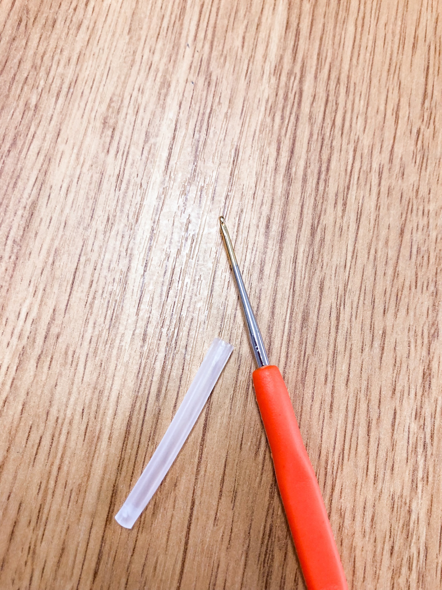 Gancho de croché com cabo vermelho e capa protetora sobre superfície de madeira