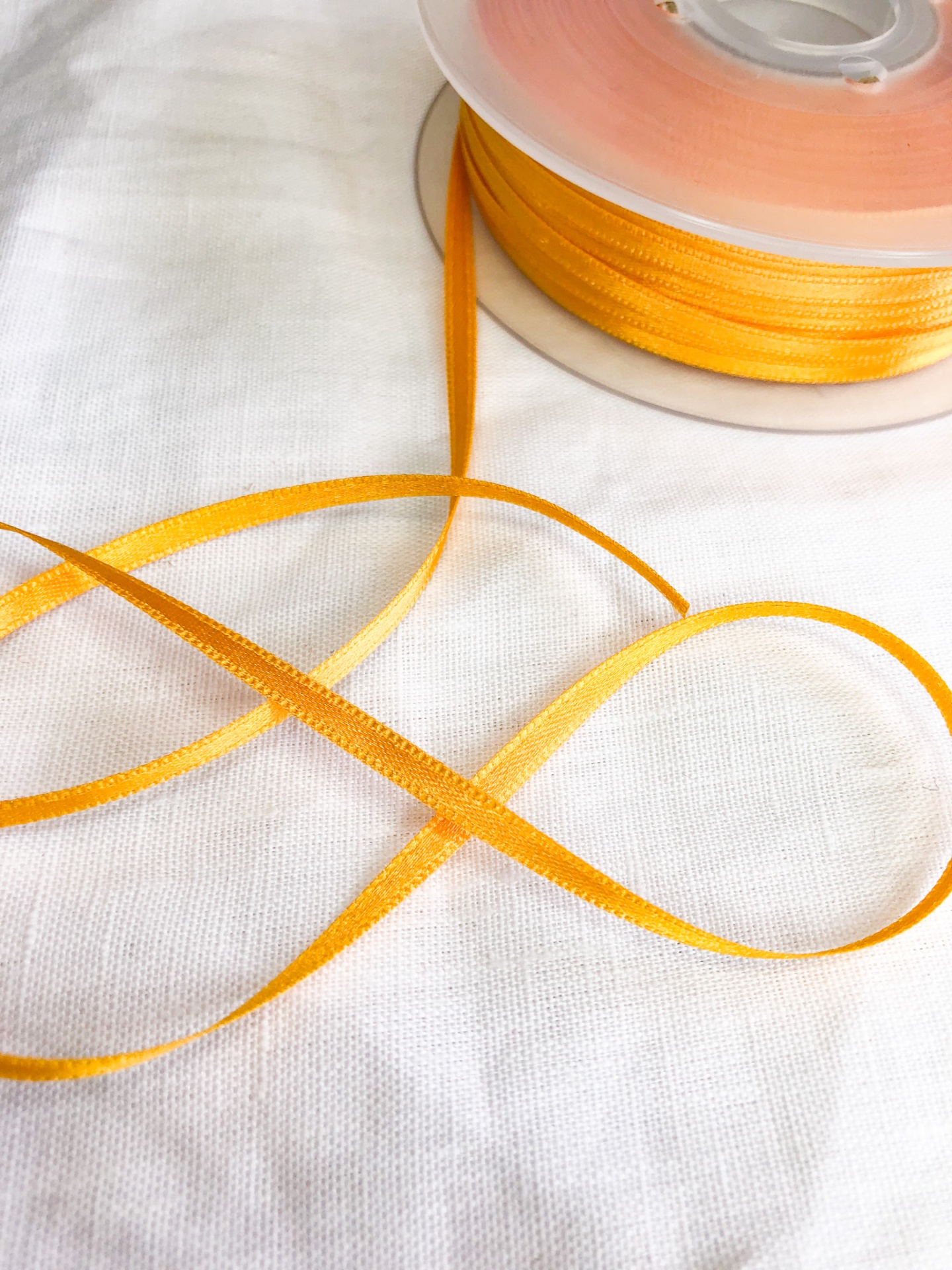 Fita estreita amarelo ouro em rolo sobre tecido branco.