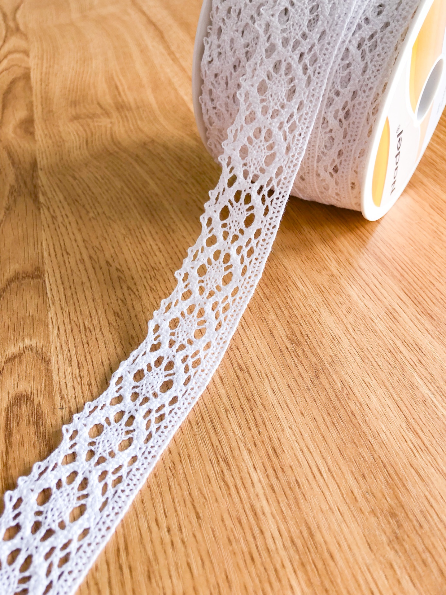 Fita de renda branca texturada enrolada em carretel sobre mesa de madeira