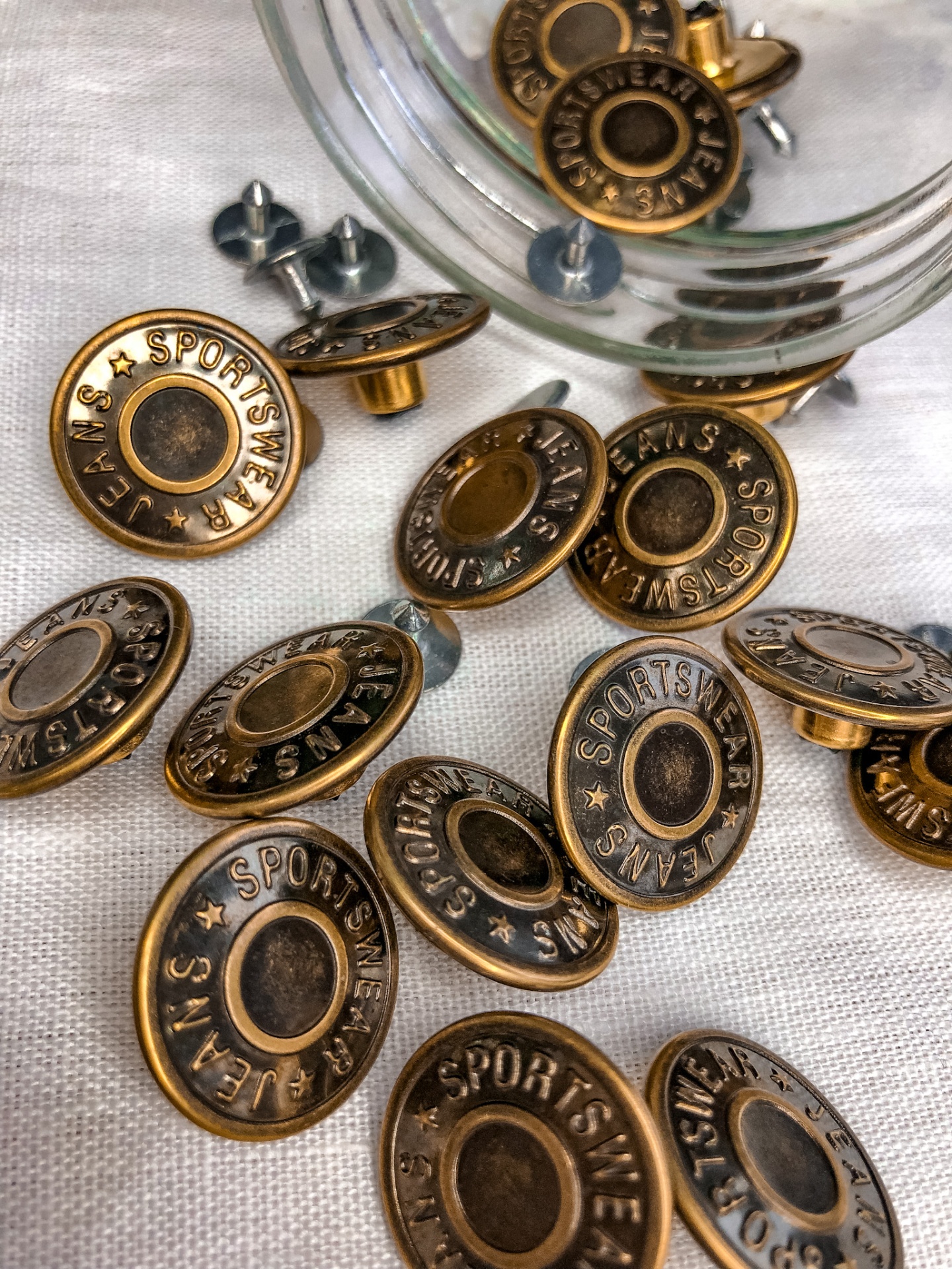 Botões metálicos redondos cor bronze com relevo e centro preto sobre tecido branco