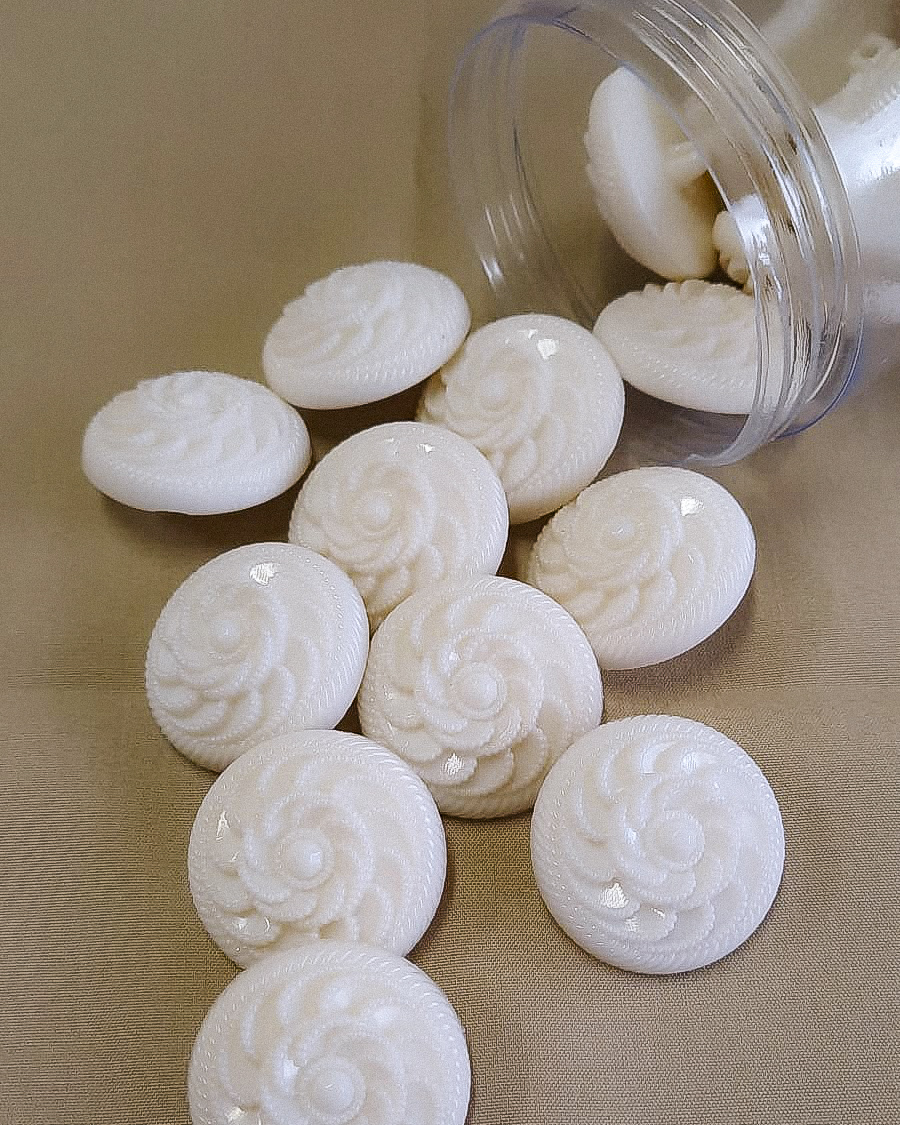 Pastilhas brancas redondas com relevo em forma de concha saindo de frasco transparente