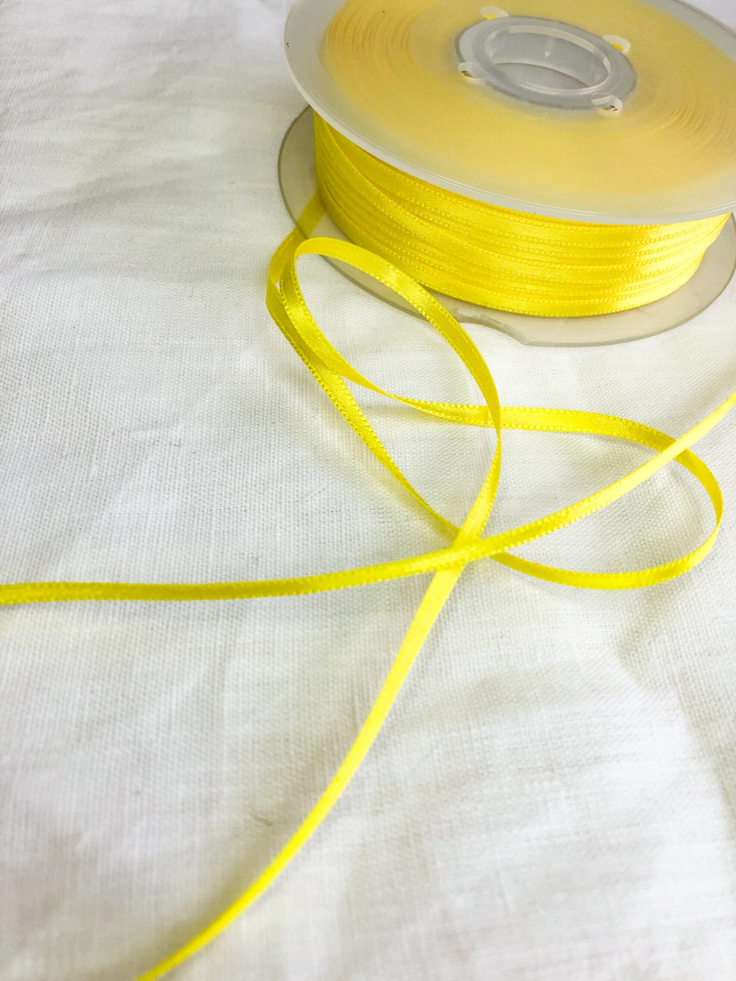 Carretel de fita amarela satinada fina sobre tecido branco