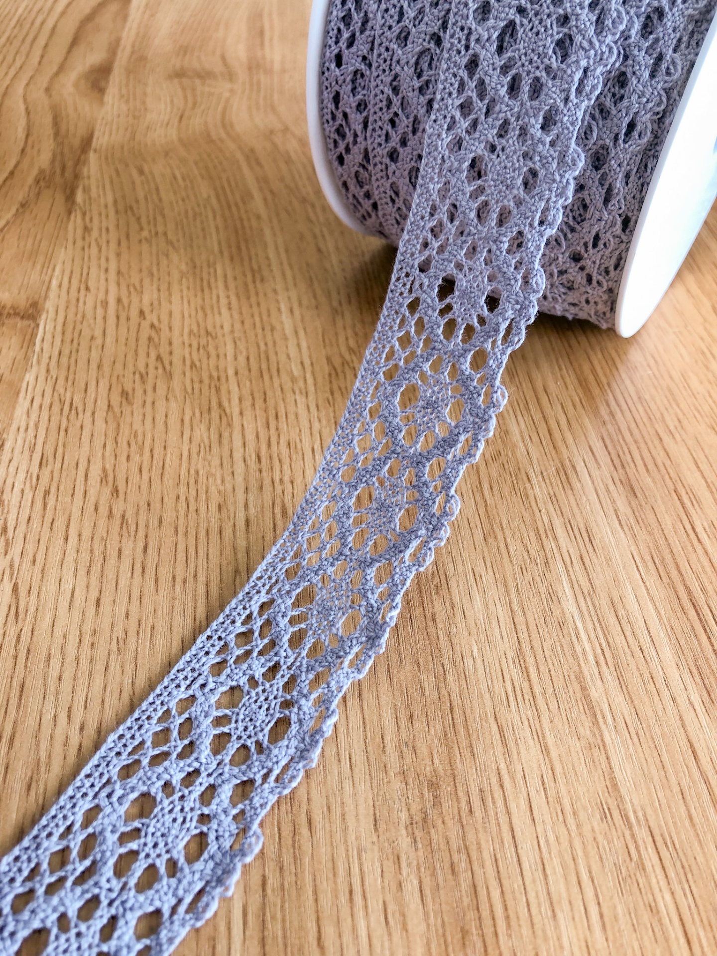 Fita de renda cinzenta com padrão floral em rolo sobre madeira clara