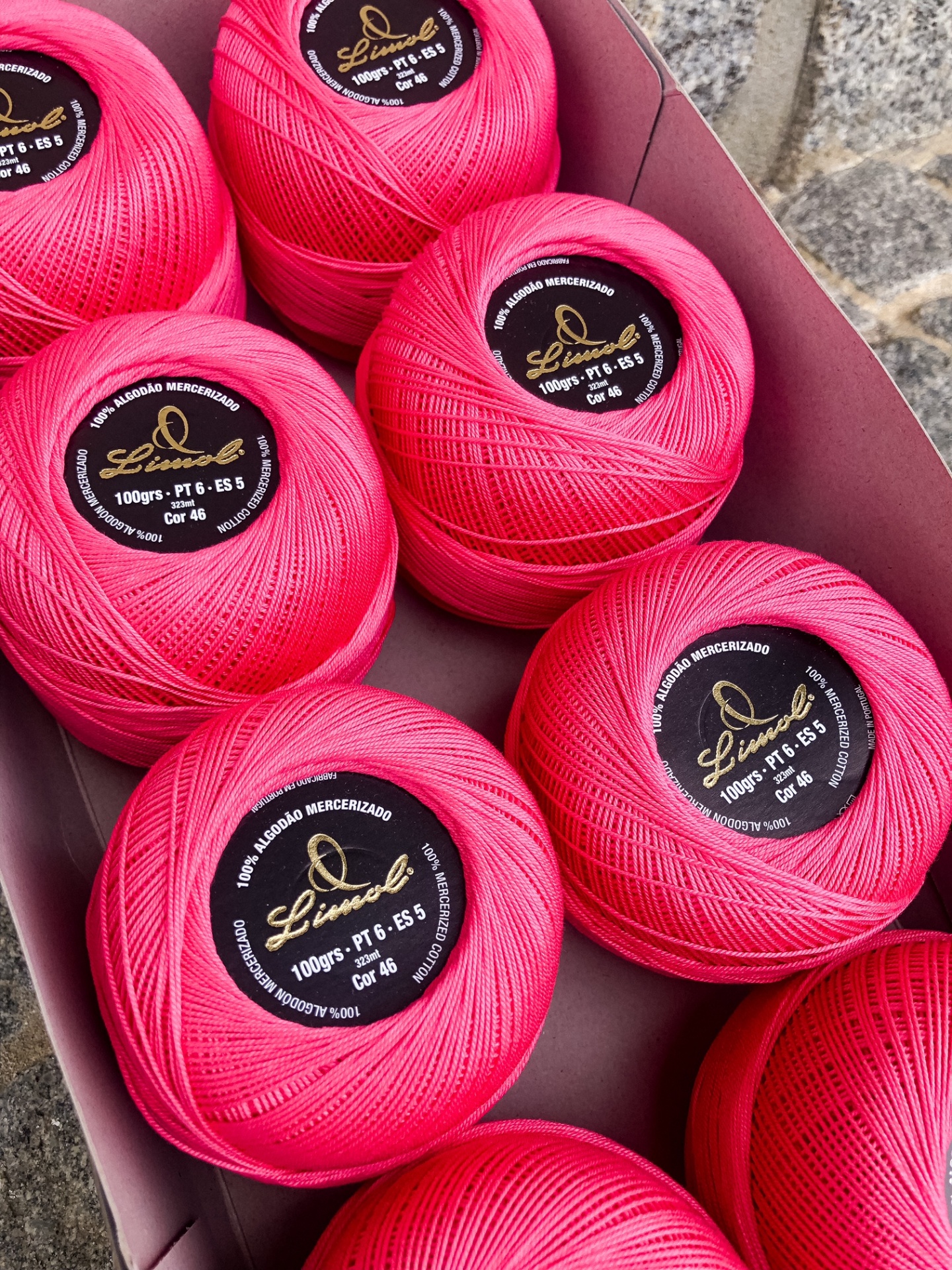 Rolos de linha rosa em caixa com etiquetas pretas detalhando especificações do produto.