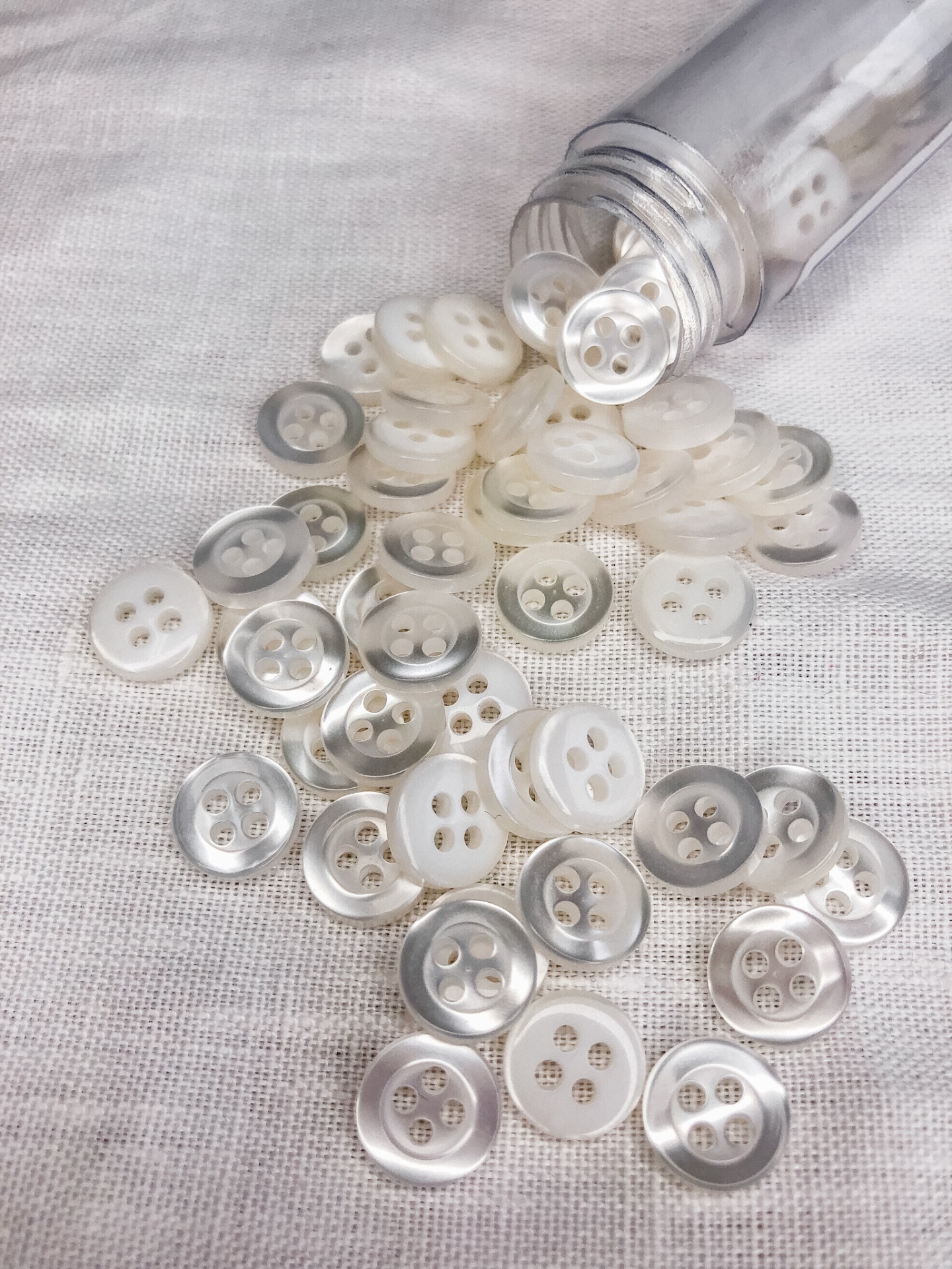 Botões redondos brancos com brilho perolado e borda prateada sobre tecido branco