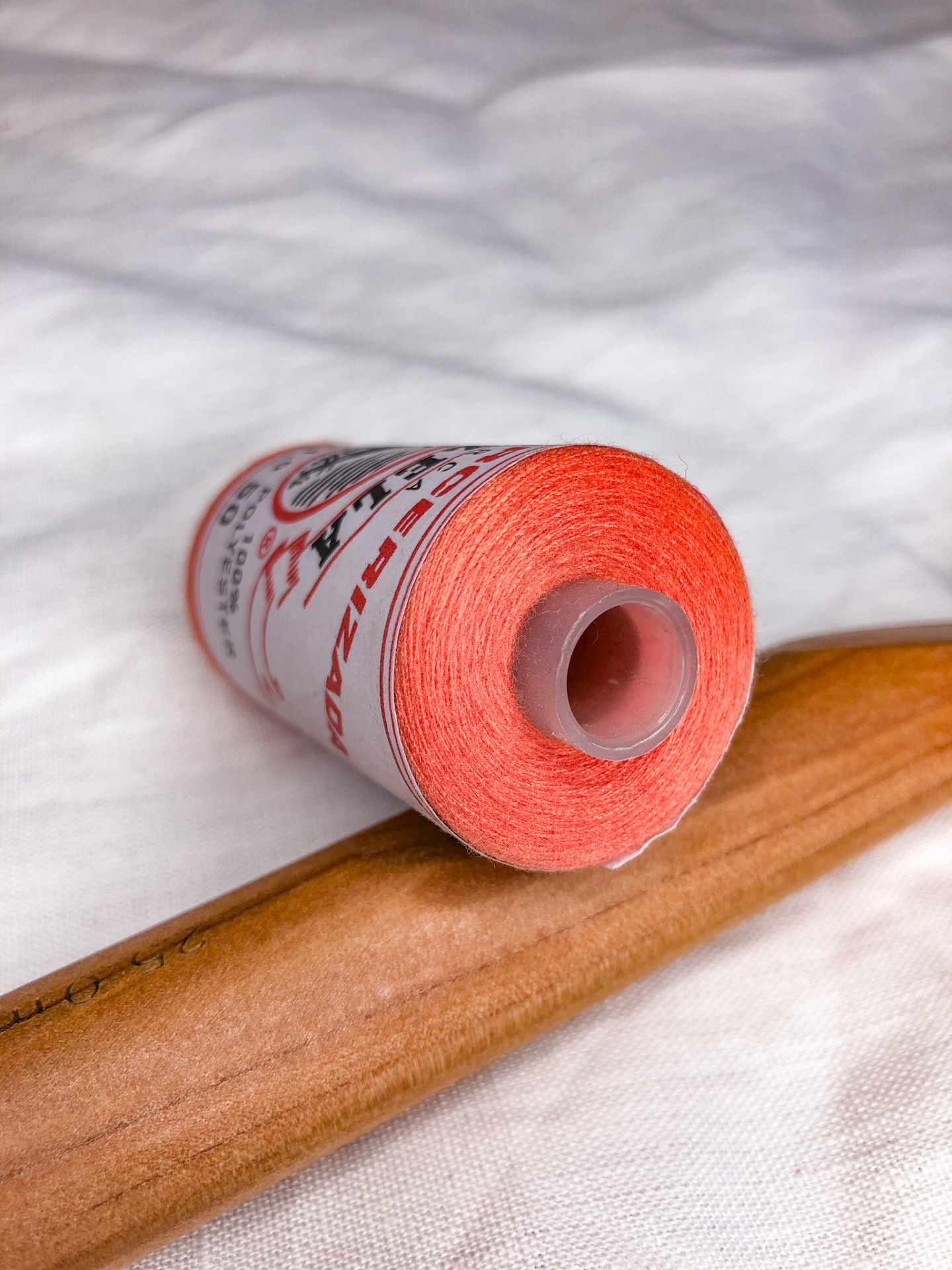 Rolo de linha cor de salmão com etiqueta e carretel cinzento sobre madeira clara e tecido branco