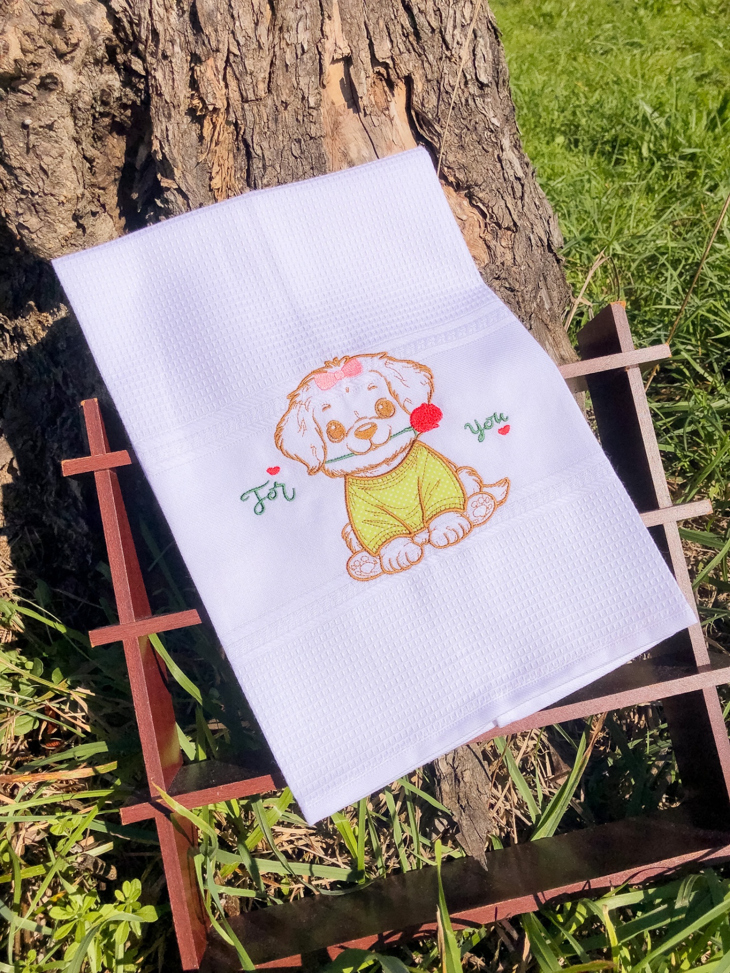 Toalha branca bordada com cão e texto 'For You' sobre estrutura de madeira ao ar livre