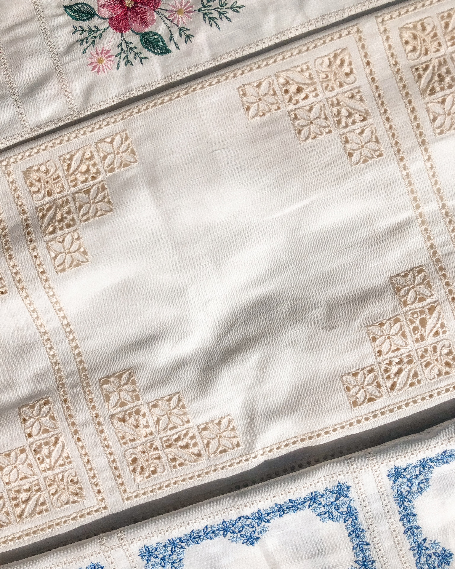 Pano de mesa branco com bordados geométricos bege e outras peças bordadas coloridas