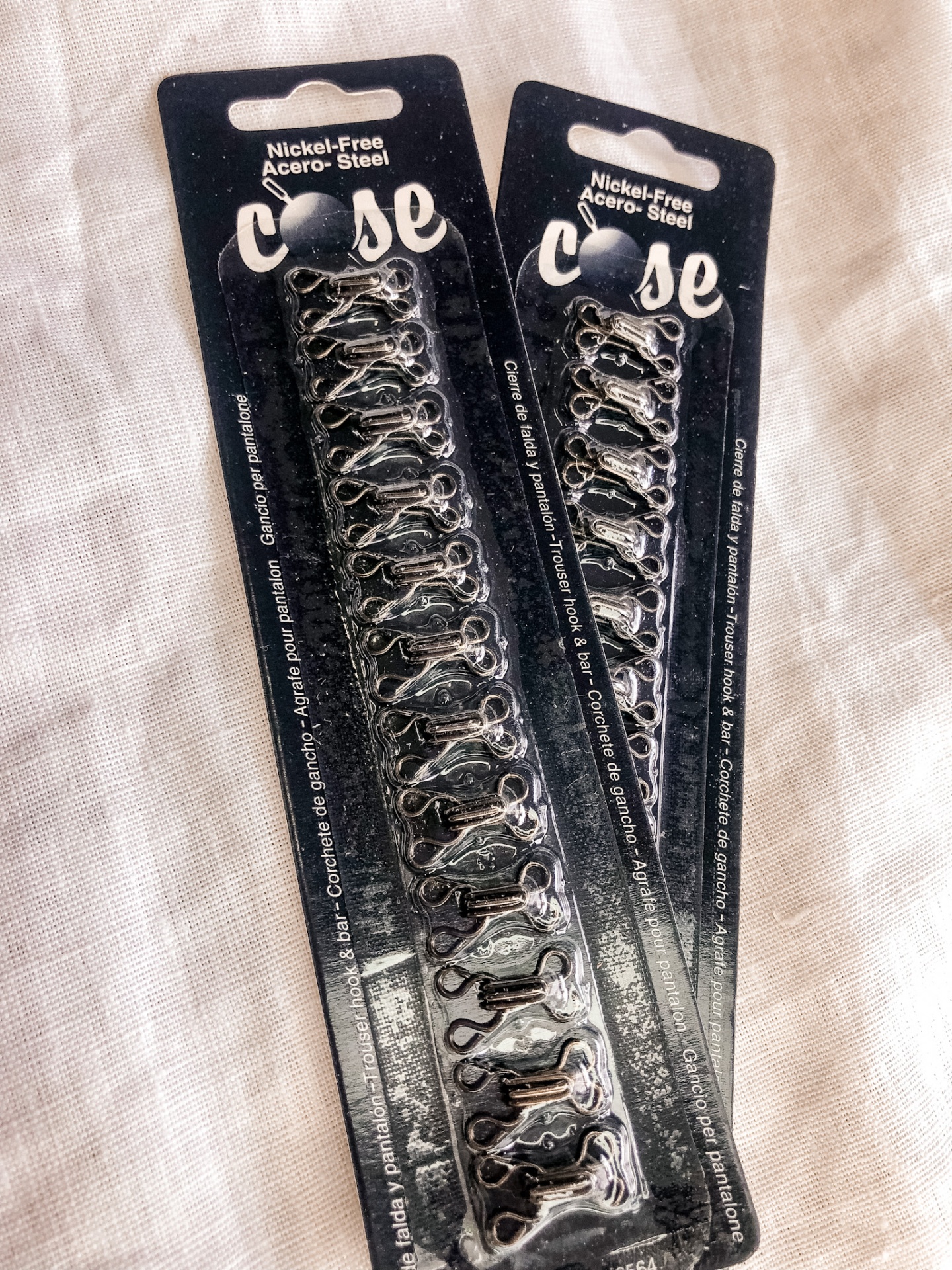 Dois pacotes de fechos em aço inoxidável prateados em cartão preto.