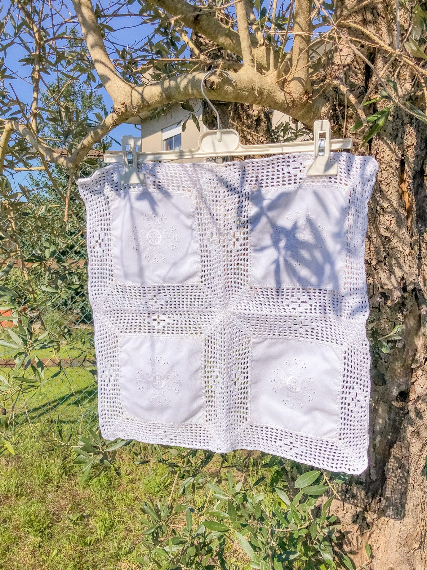 Guarda de croché branca quadrada pendurada numa árvore numa zona ajardinada