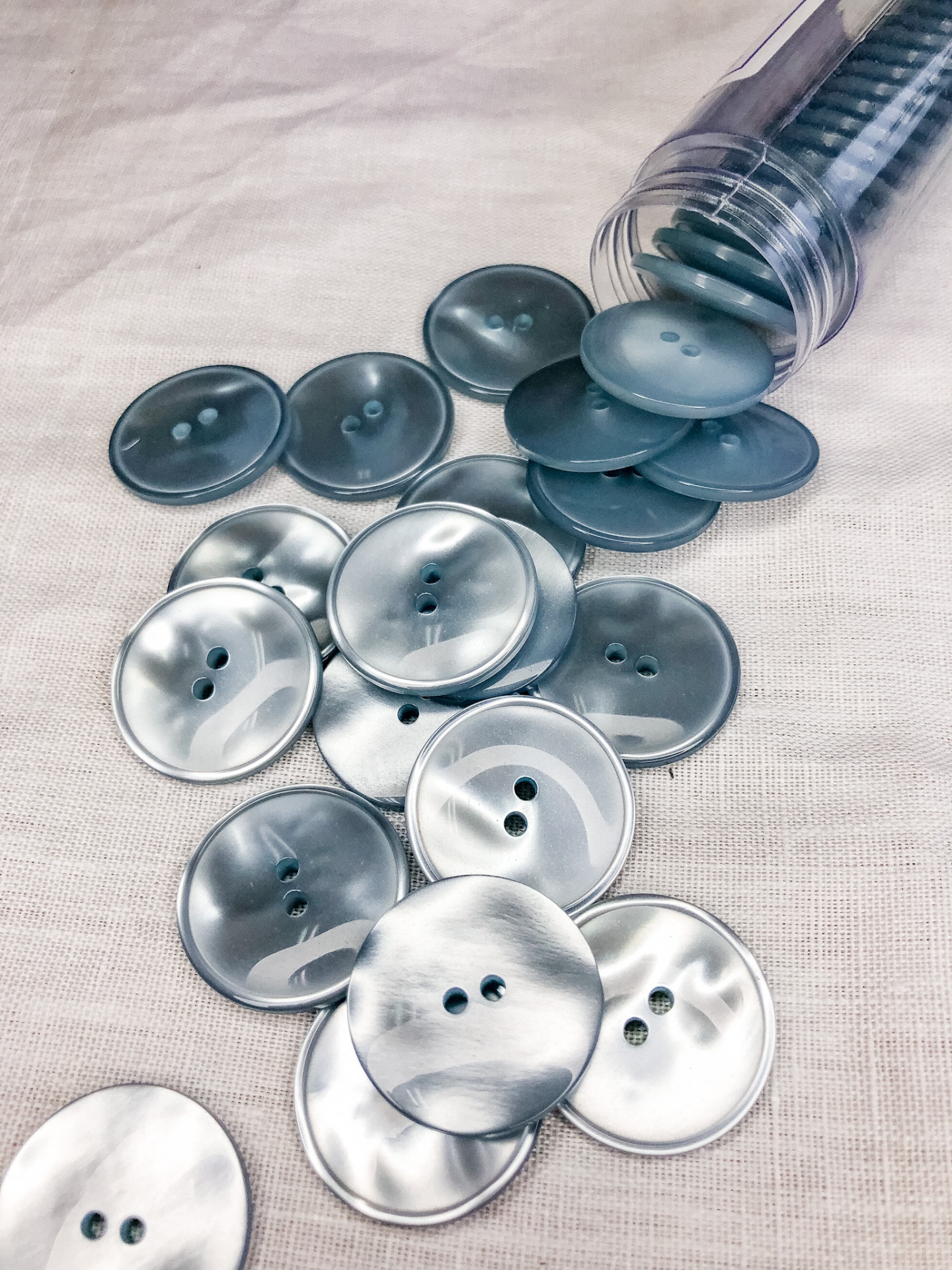 Botões plásticos prateados com dois furos e recipiente plástico transparente