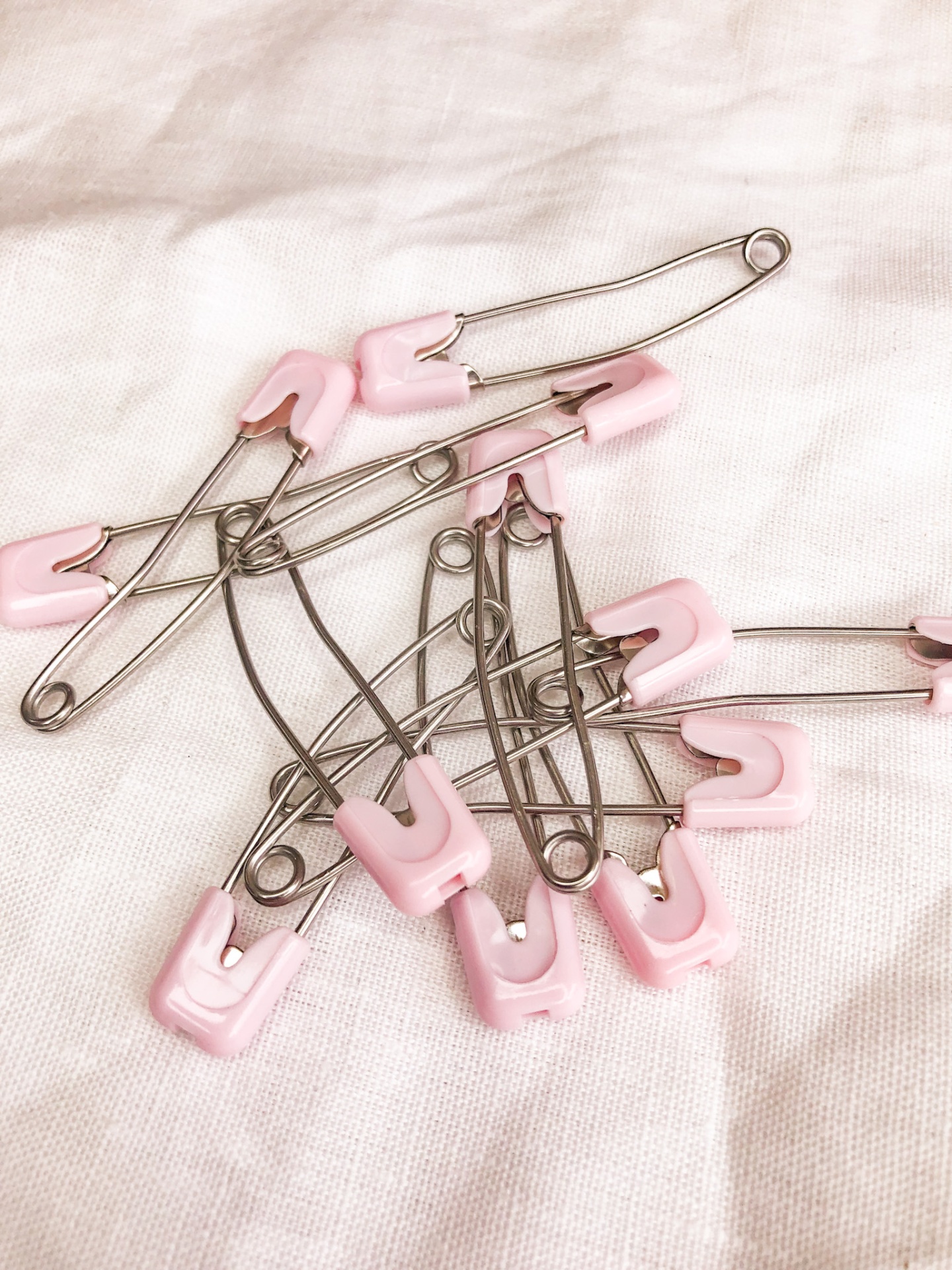 Alfinetes de segurança metálicos com tampas cor-de-rosa sobre tecido branco
