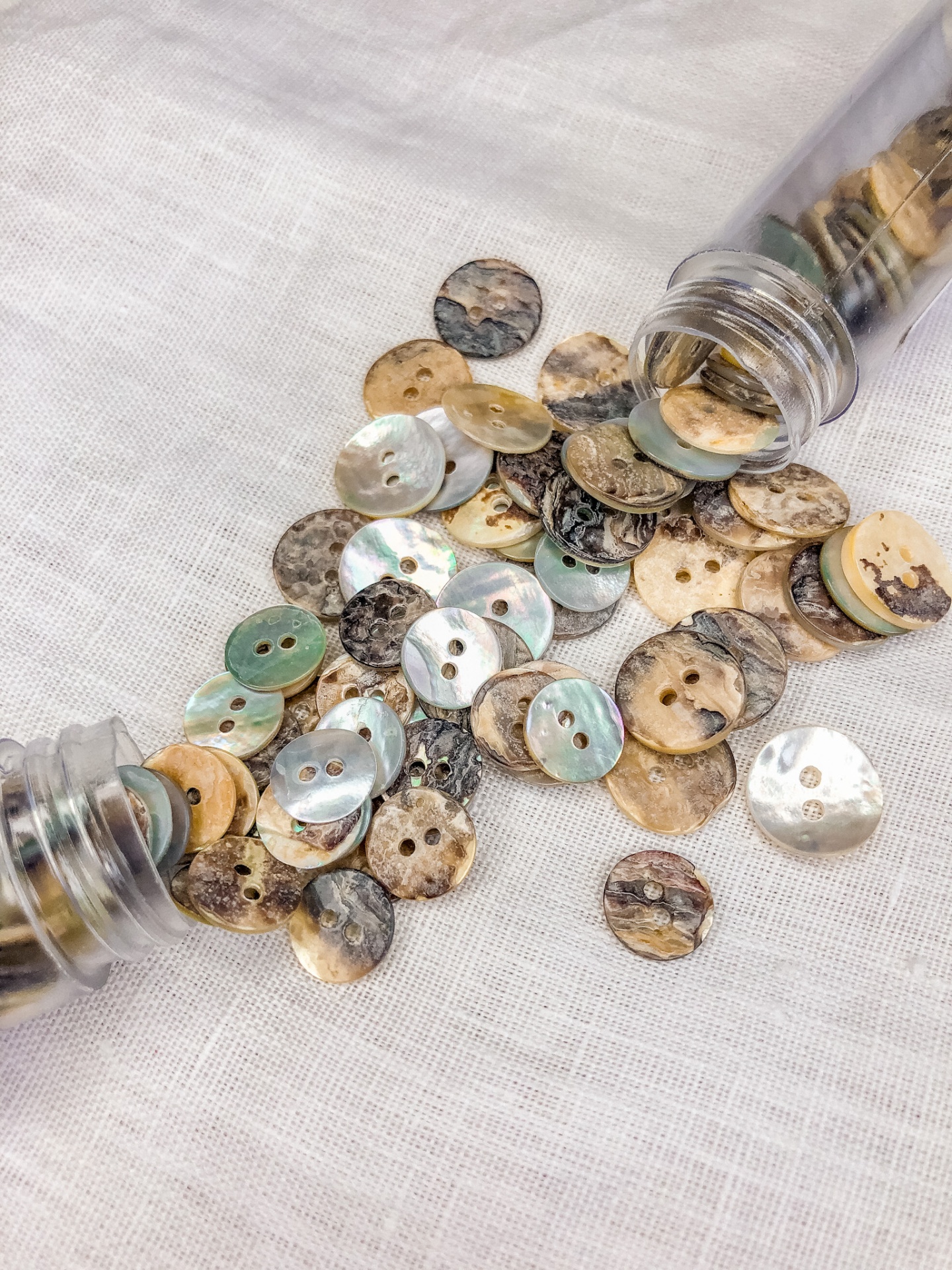 Botões naturais coloridos em tecido branco com dois frascos de vidro.