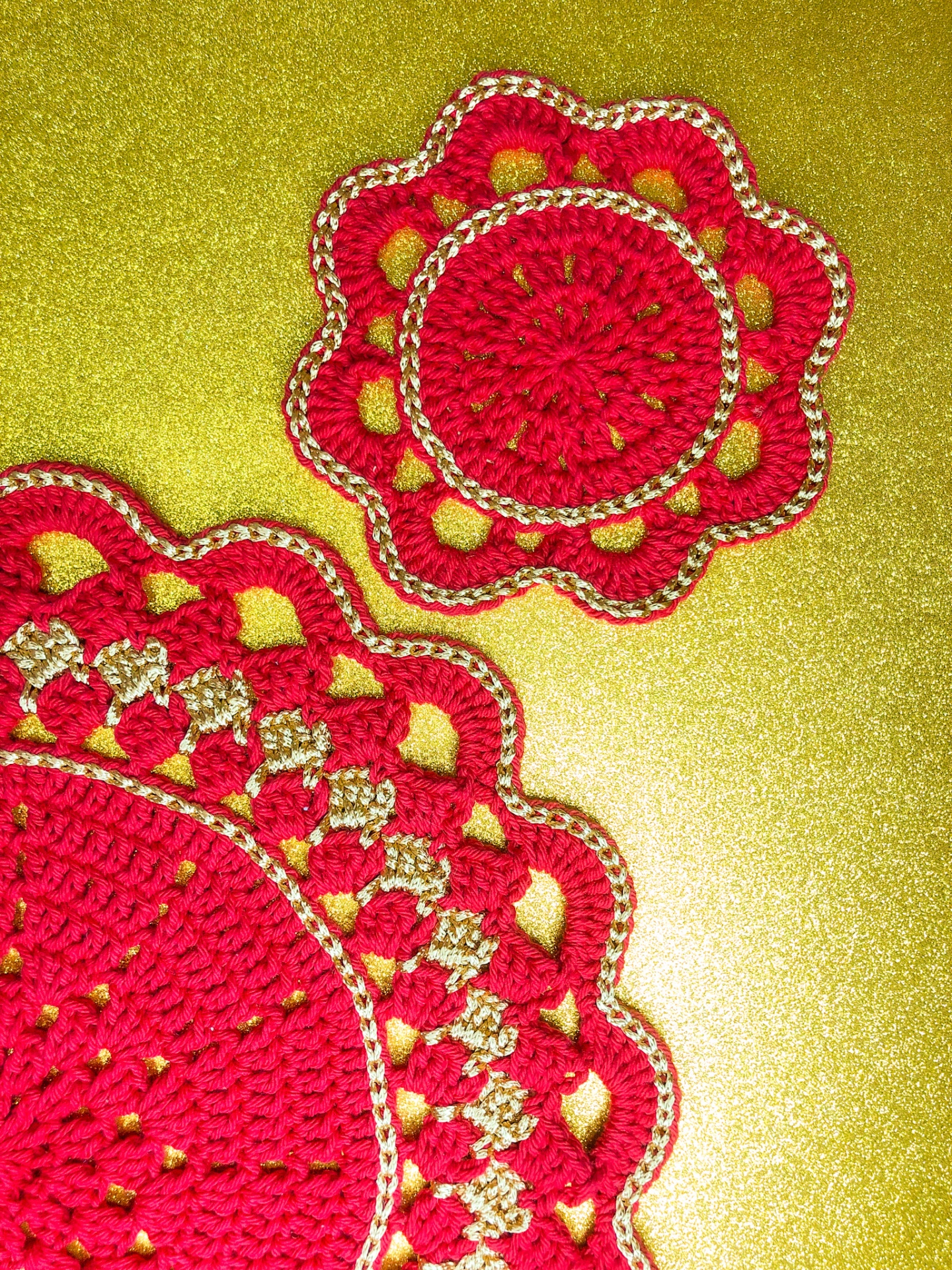 Apontadores redondos de crochê vermelhos e dourados sobre superfície brilhante.