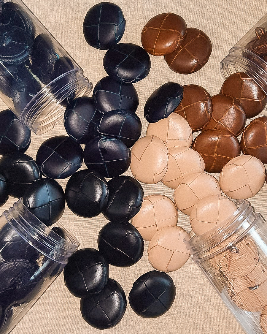 Bolas de couro preto, castanho e bege espalhadas e em frascos de plástico transparente.