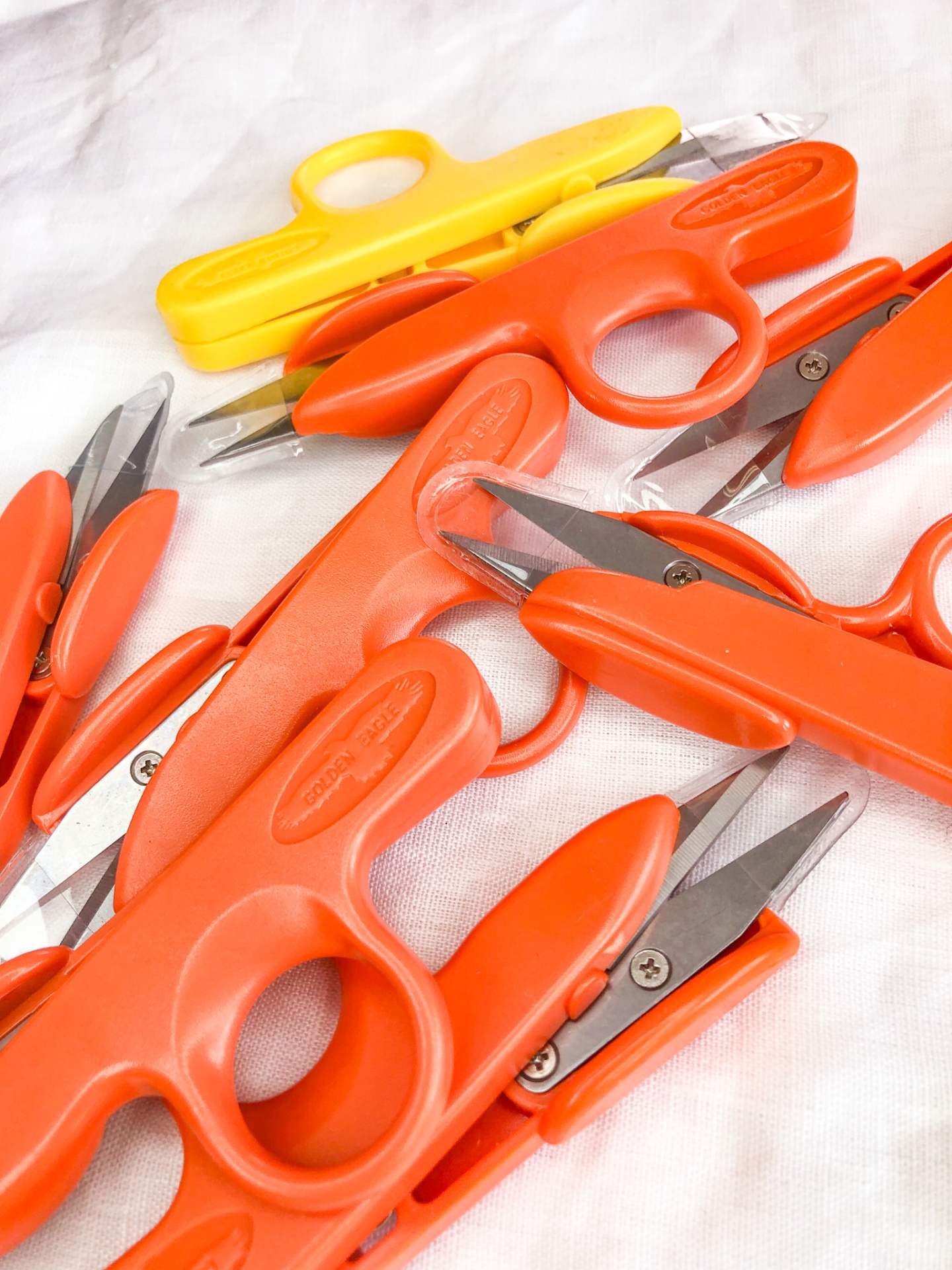 Tesouras pequenas laranjas e amarelas com lâminas metálicas sobre tecido branco