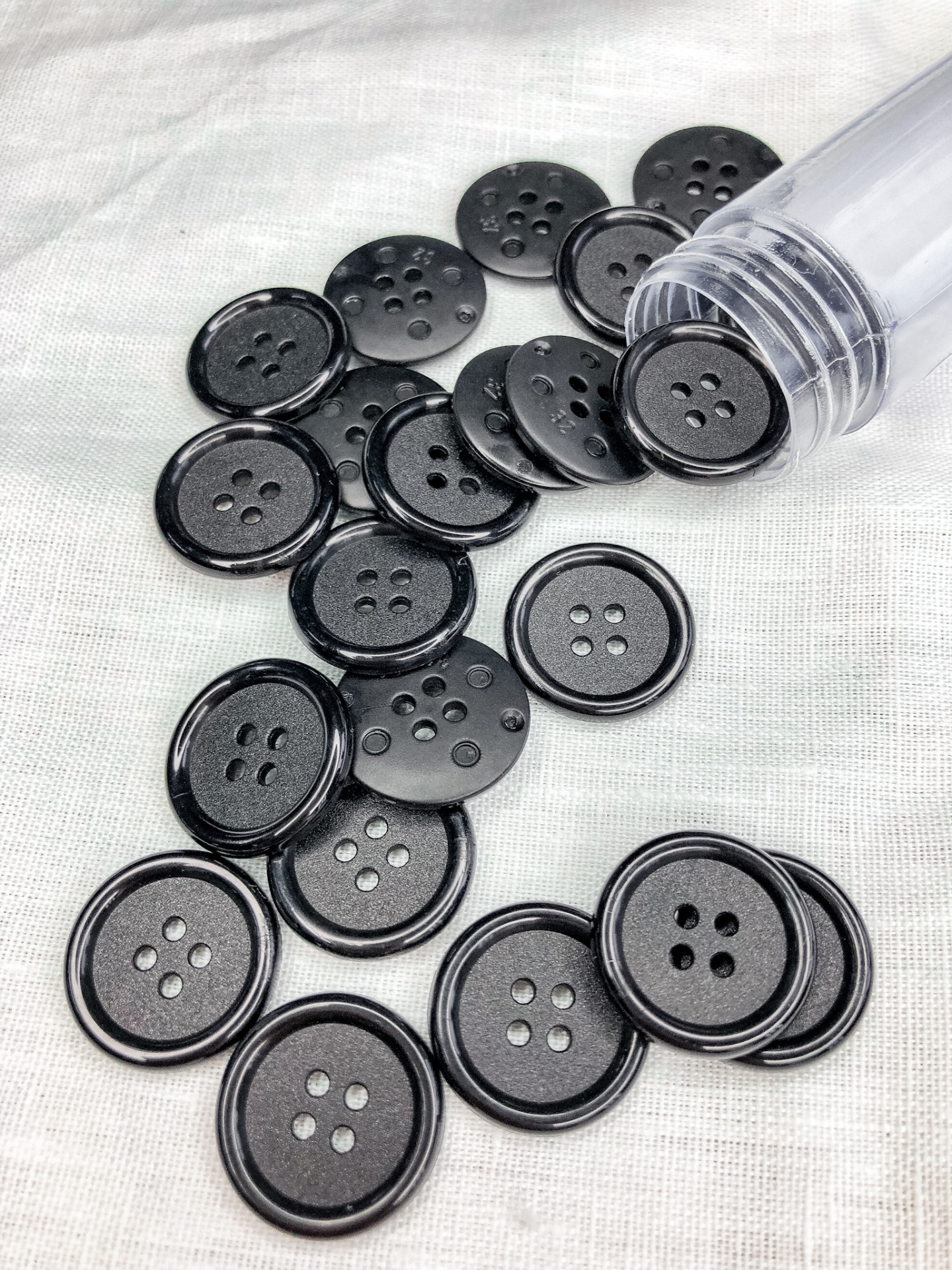 Botões pretos redondos com quatro furos sobre tecido cinzento