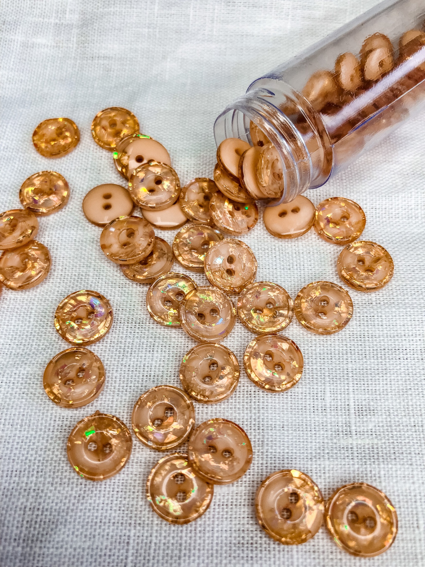 Botões laranja transparentes brilhantes espalhados e frasco plástico aberto sobre tecido branco