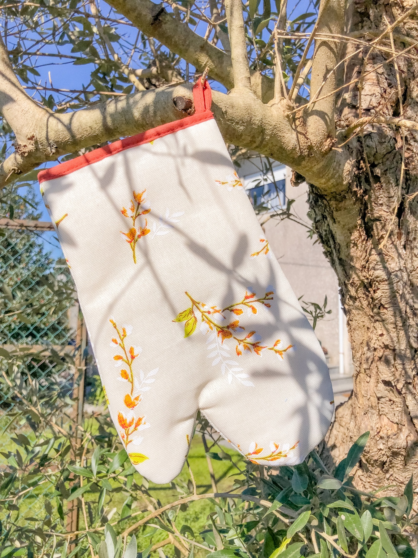 Luva de forno branca com flores amarelas pendurada numa árvore