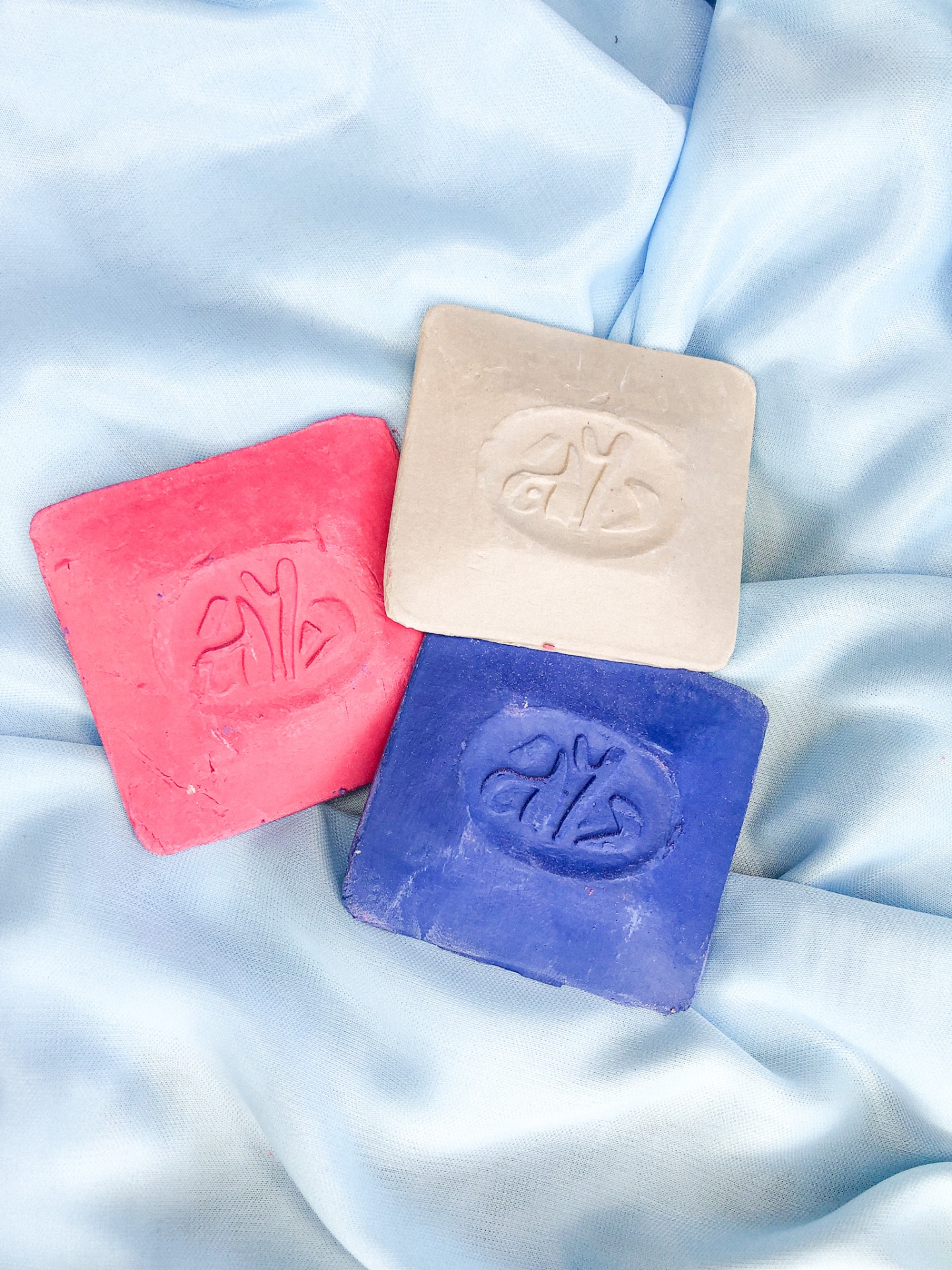 Três barras de sabão quadradas vermelha, branca e azul sobre tecido azul claro