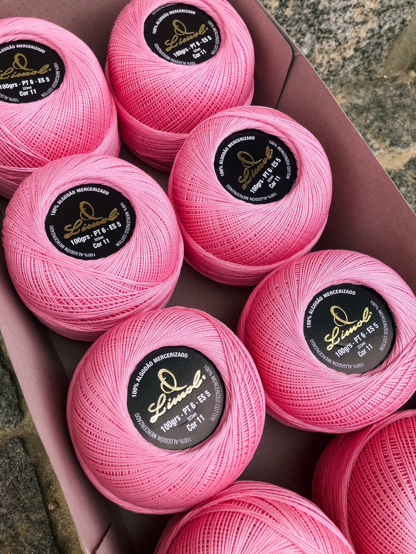 Novelos de linha cor-de-rosa com rótulos pretos e dourados dentro de caixa de cartão.