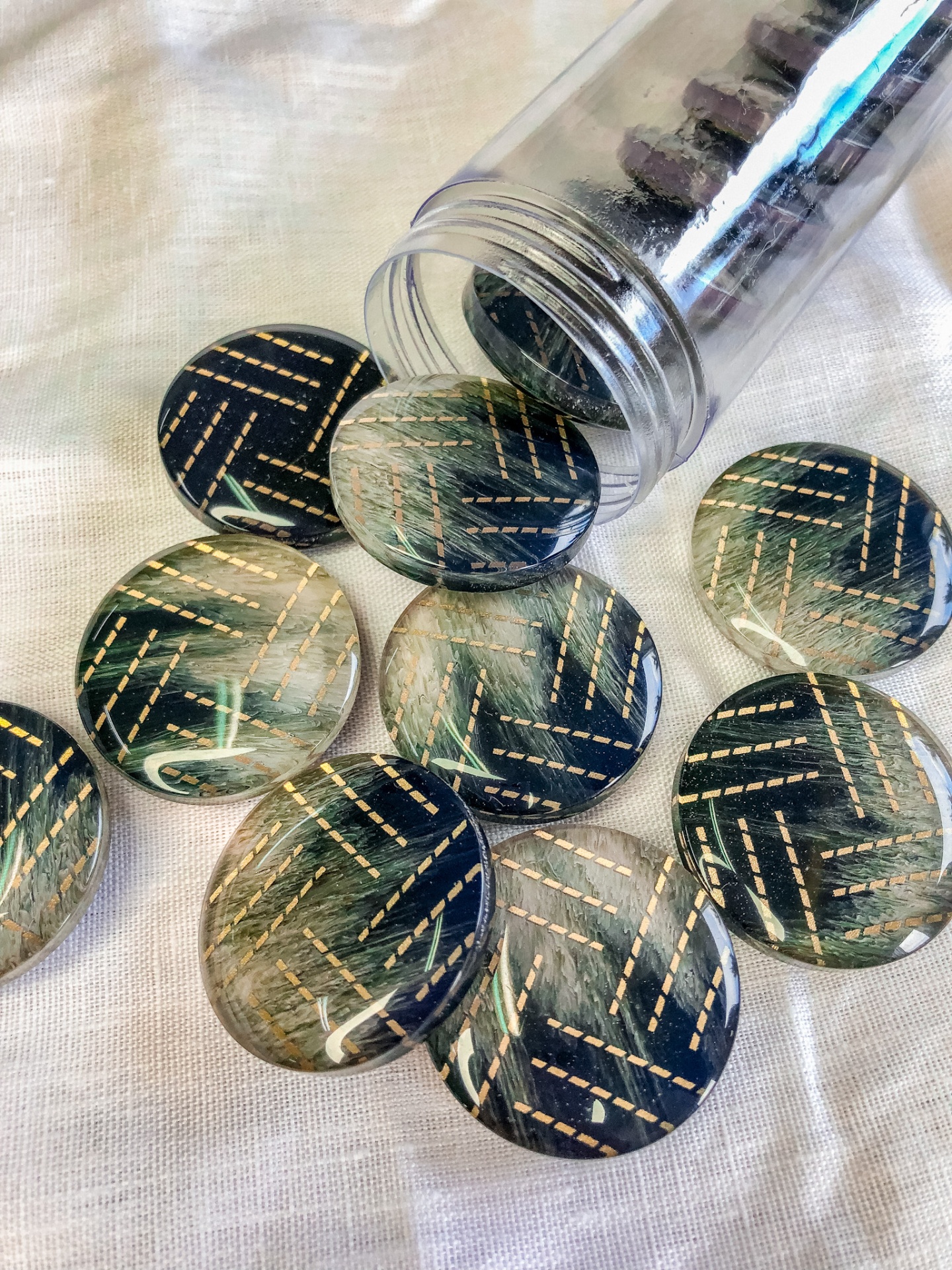 Pedras decorativas azuis e verdes com padrão dourado num frasco plástico transparente