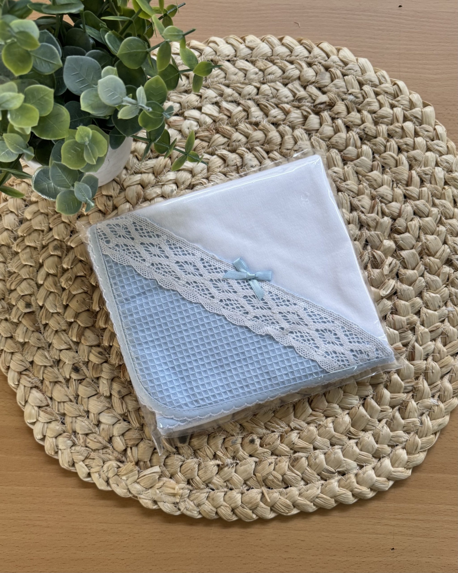 Fralda de bebé branca e azul com renda e laço sobre tapete trançado