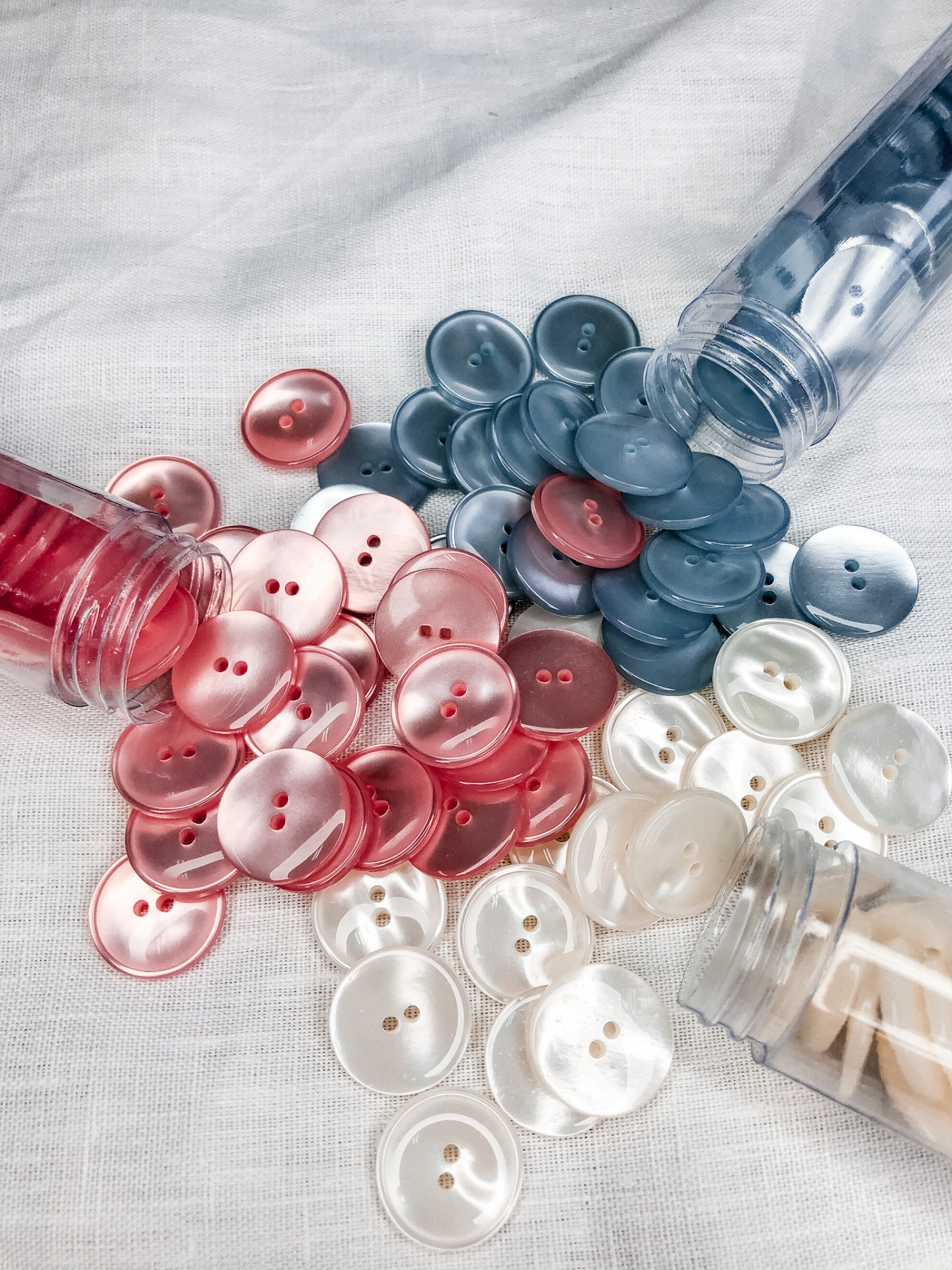 Botões redondos de plástico em vermelho, azul e branco perolado, com dois furos, em tecido branco