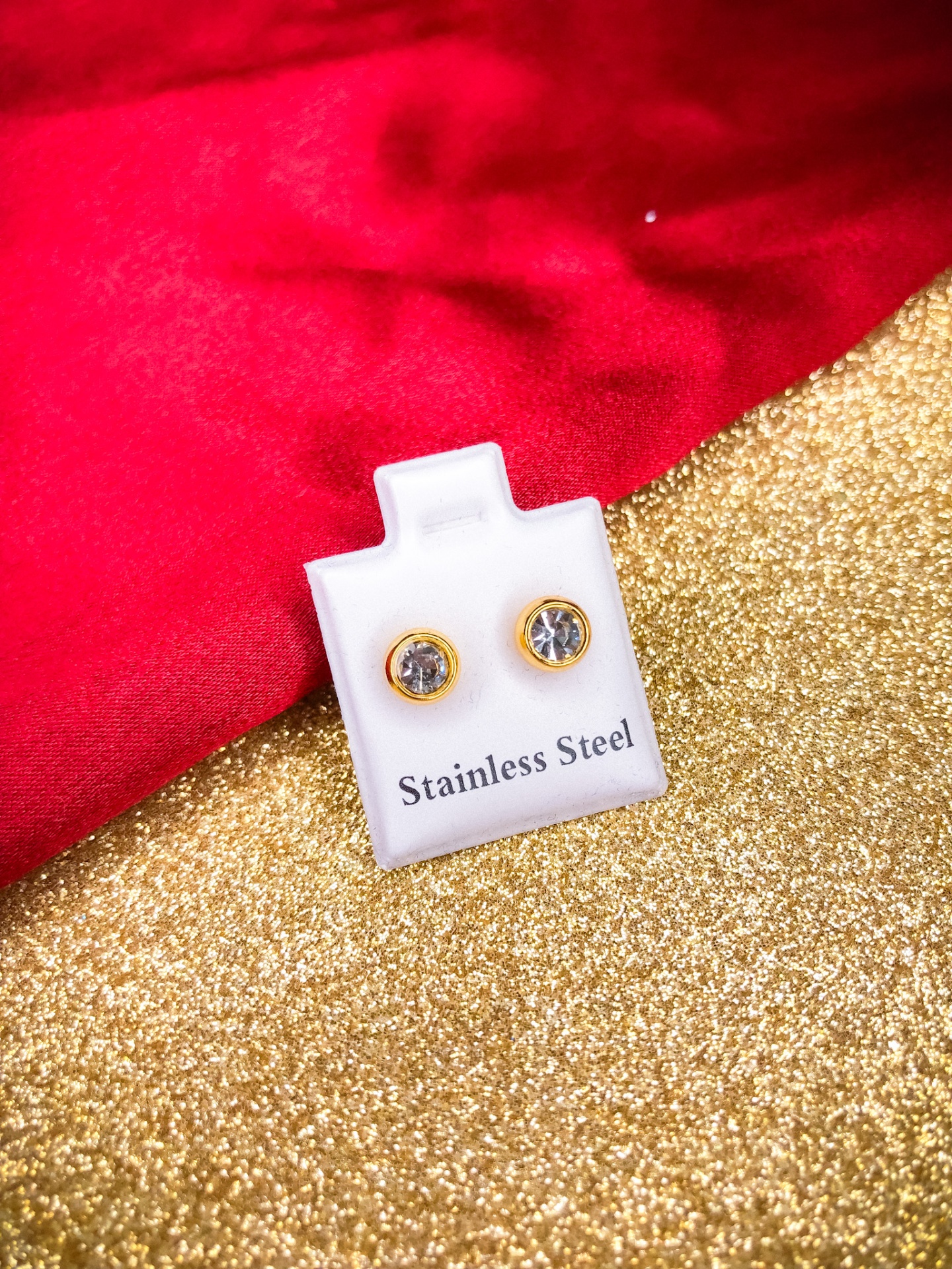 Brincos de aço inoxidável com pedra transparente e aro dourado em suporte branco com texto 'Stainless Steel'