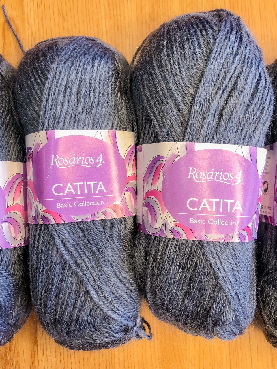 Novelos de lã cinzenta escura Rosários 4 coleção Catita com rótulo roxo sobre madeira clara