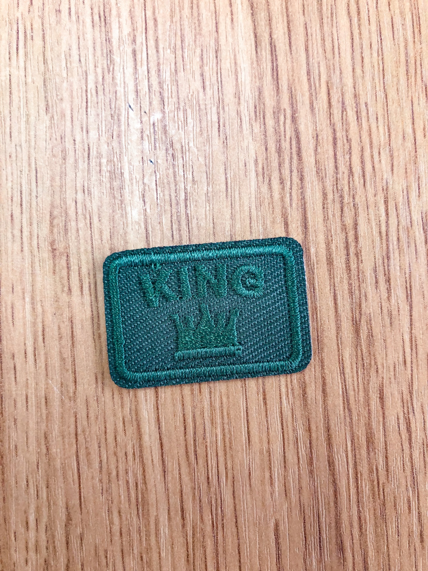 Etiqueta verde em tecido com bordado KING e coroa