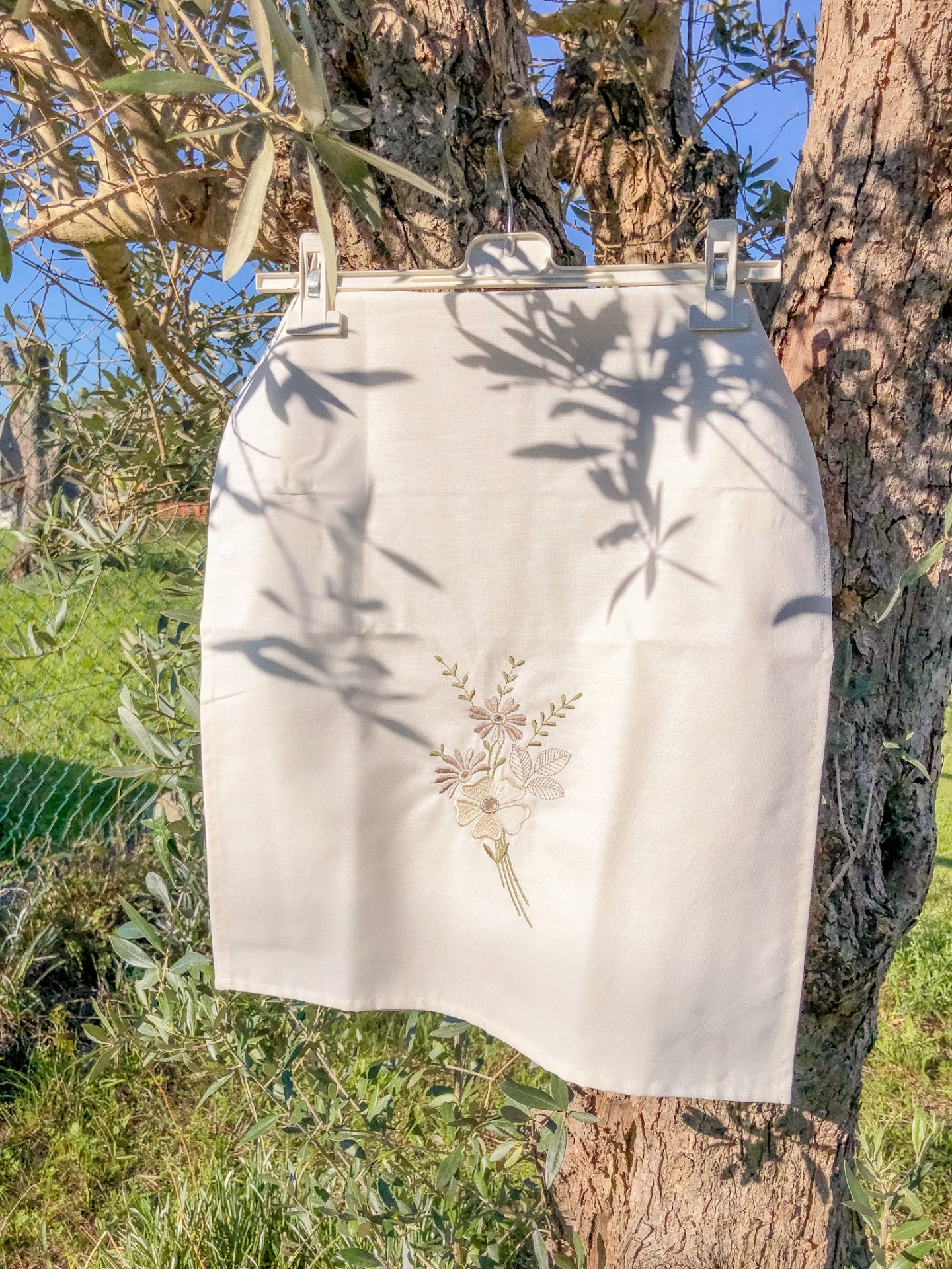 Saia branca com bordado floral pendurada numa árvore ao ar livre