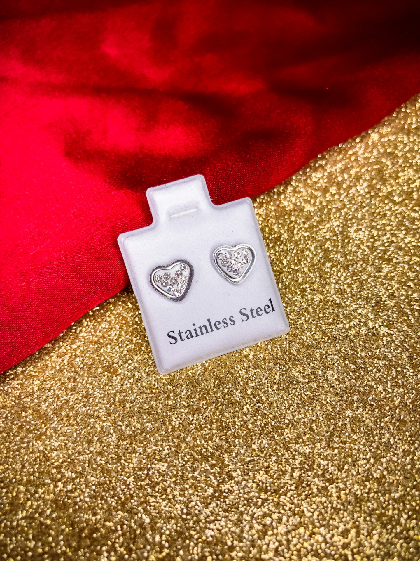 Brincos de aço inoxidável em formato de coração com brilhantes em suporte branco