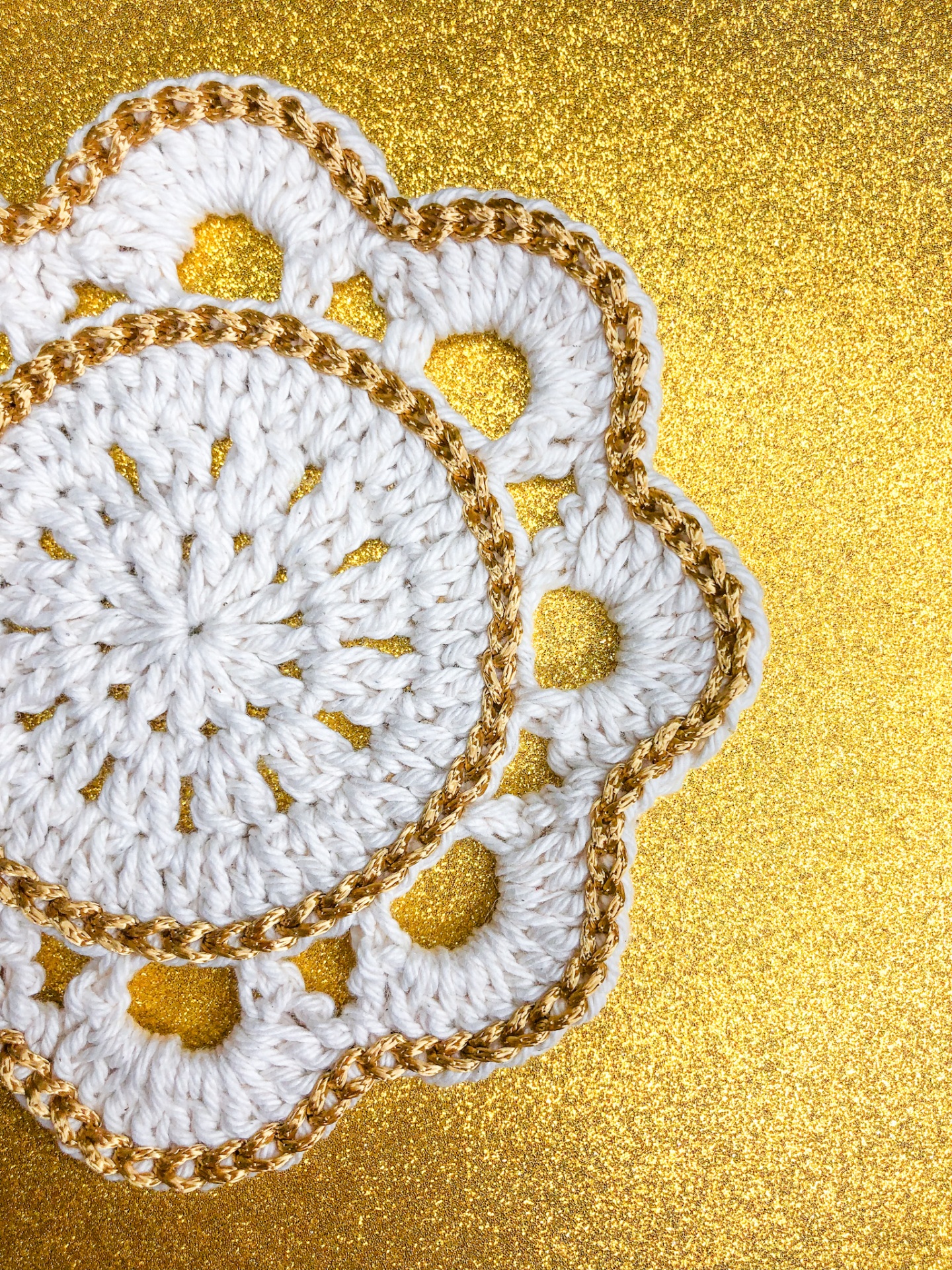 Sousplat de croché branco com bordas douradas sobre fundo dourado brilhante