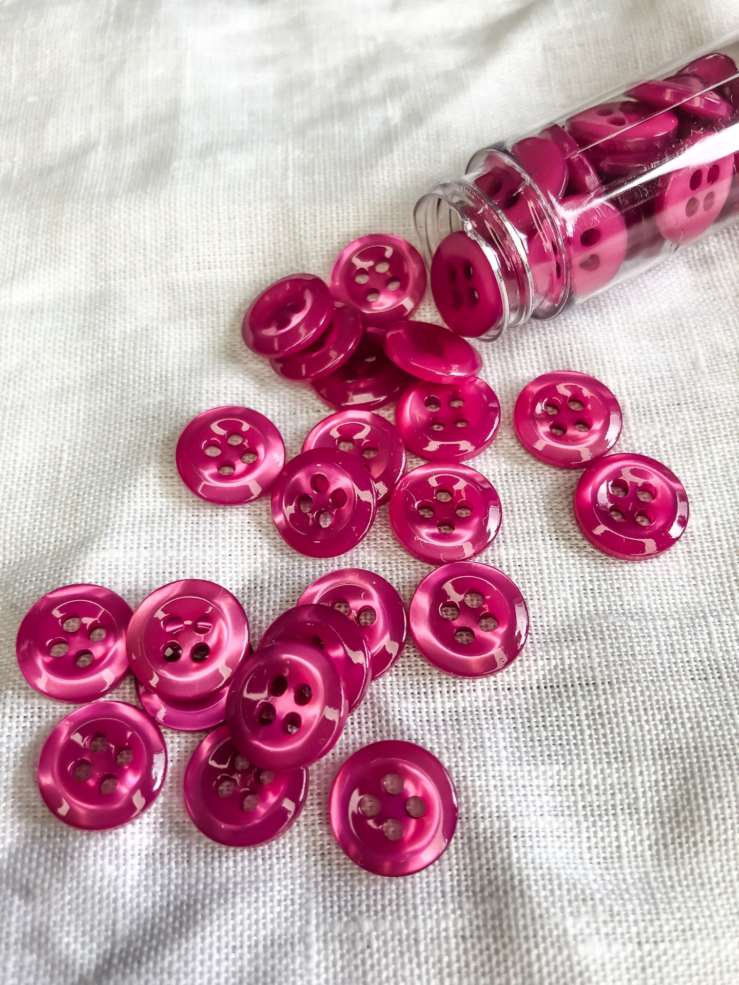 Botões cor-de-rosa brilhante com quatro furos sobre tecido branco