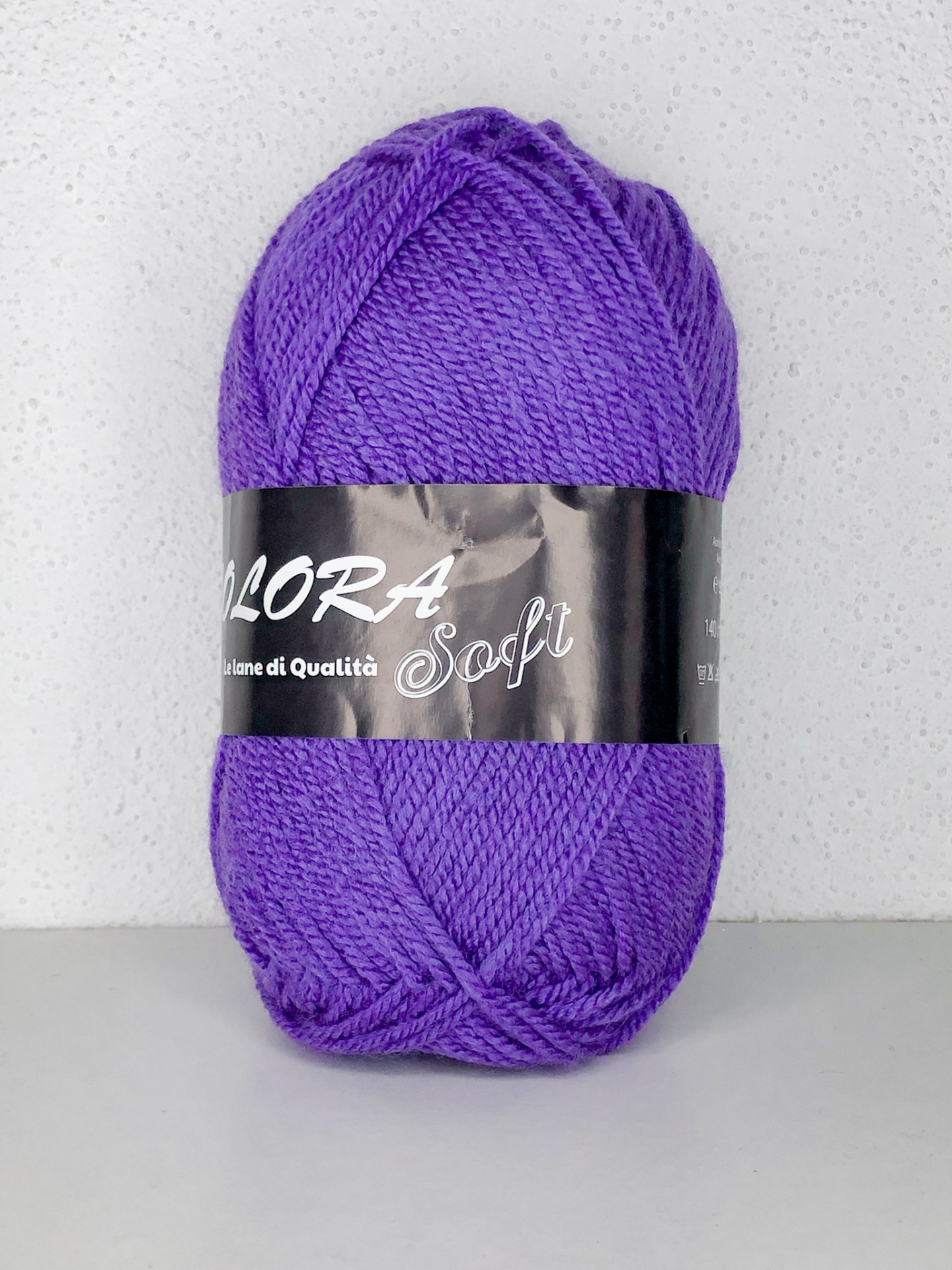 Novelo de lã roxa com etiqueta preta e texto FLORA Soft sobre fundo claro