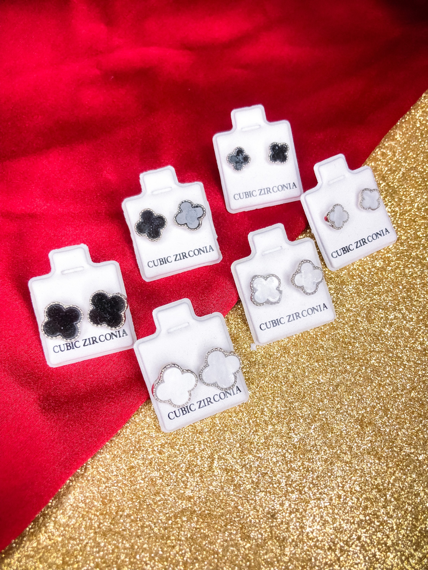 Seis pares de brincos de zircónia cúbica em suportes brancos sobre fundo vermelho e dourado glitter