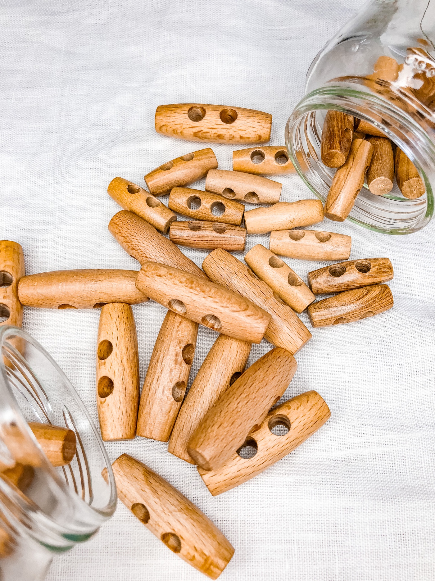 Botões de madeira cilíndricos com furos sobre tecido branco e dentro de frascos de vidro