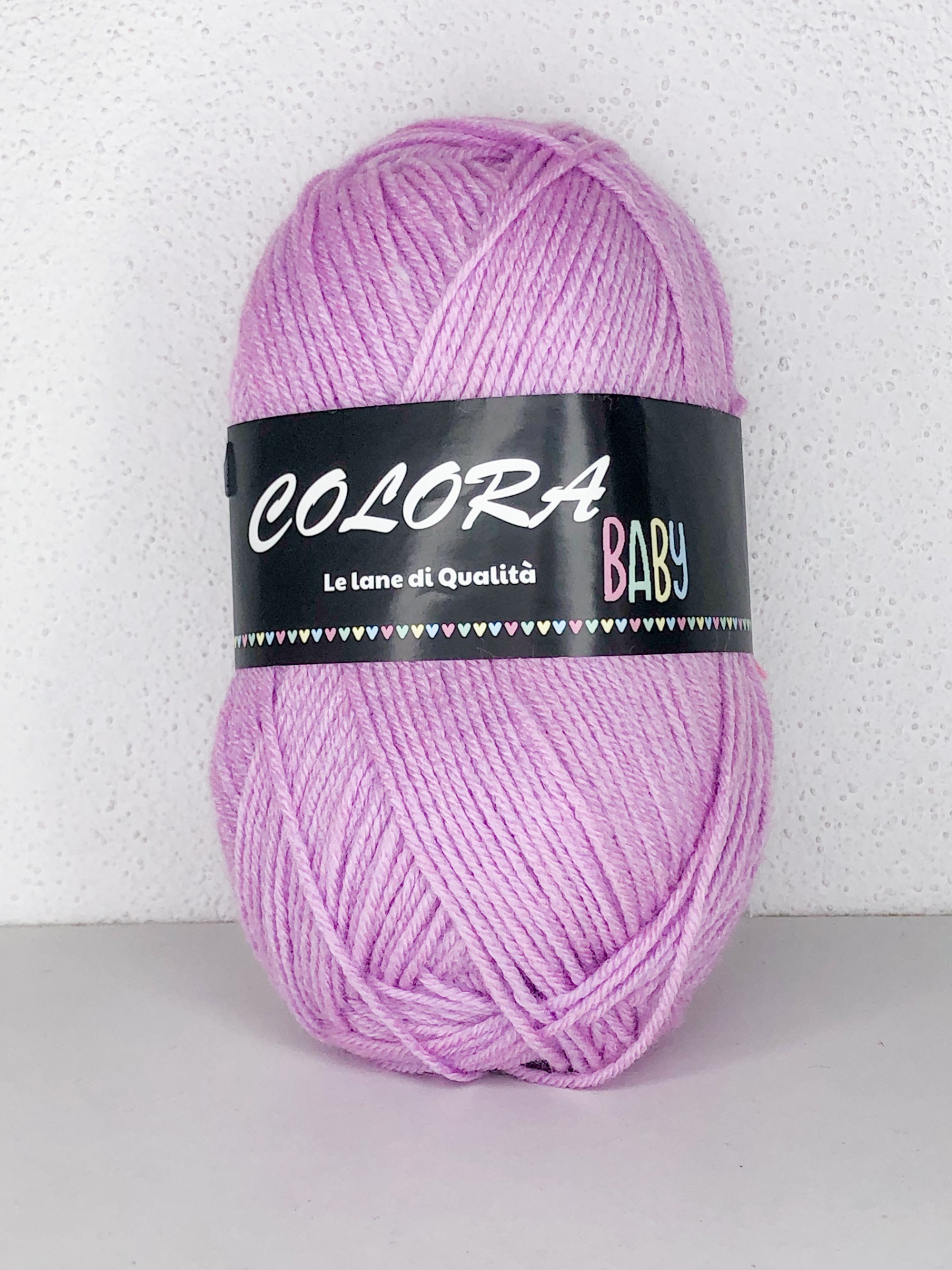 Novelo de lã rosa claro com rótulo preto COLORA BABY sobre superfície branca